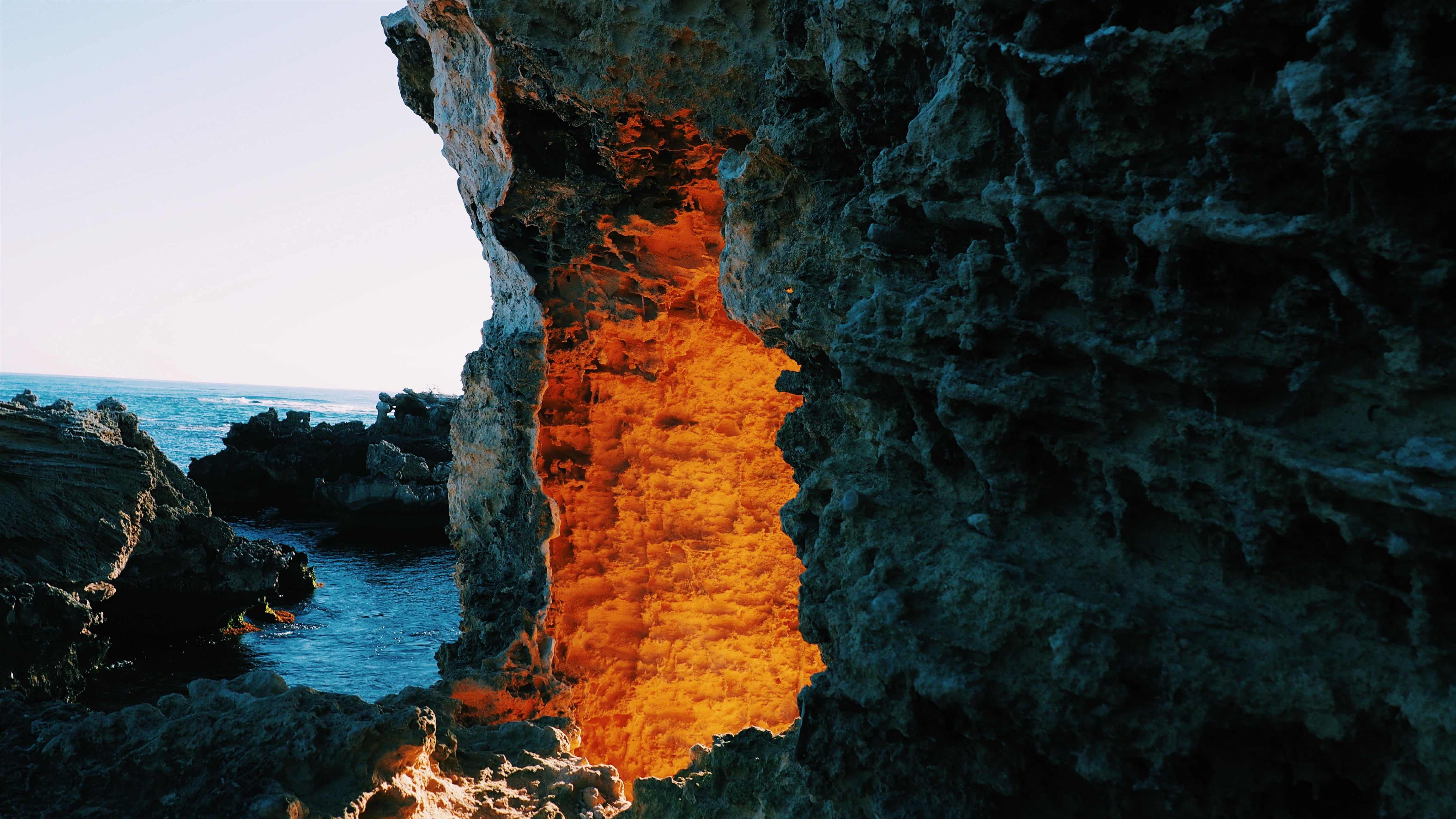 Cave opening with orange light and ocean view HD Wallpaper