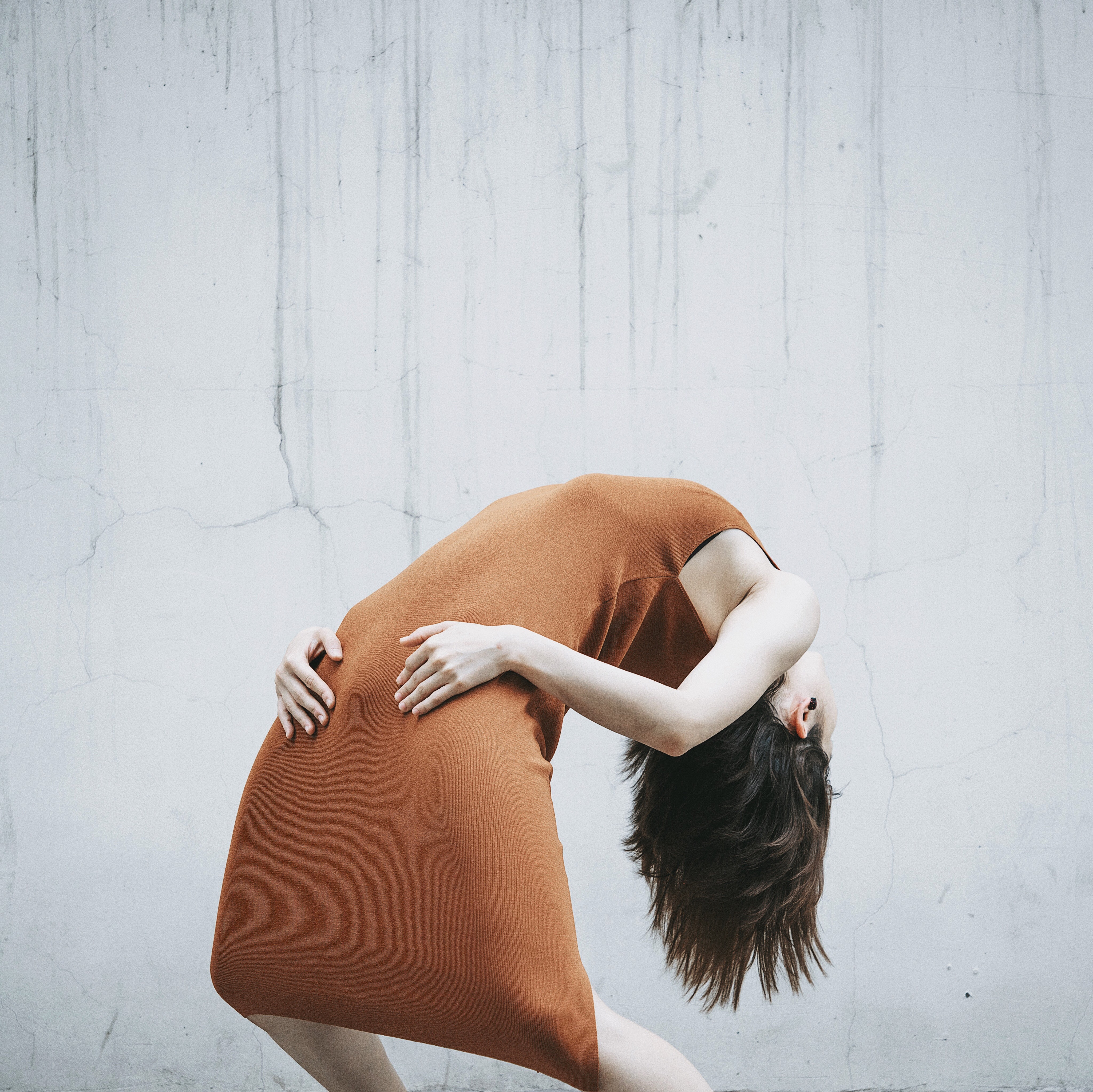 Woman in orange dress bending against a wall HD Wallpaper