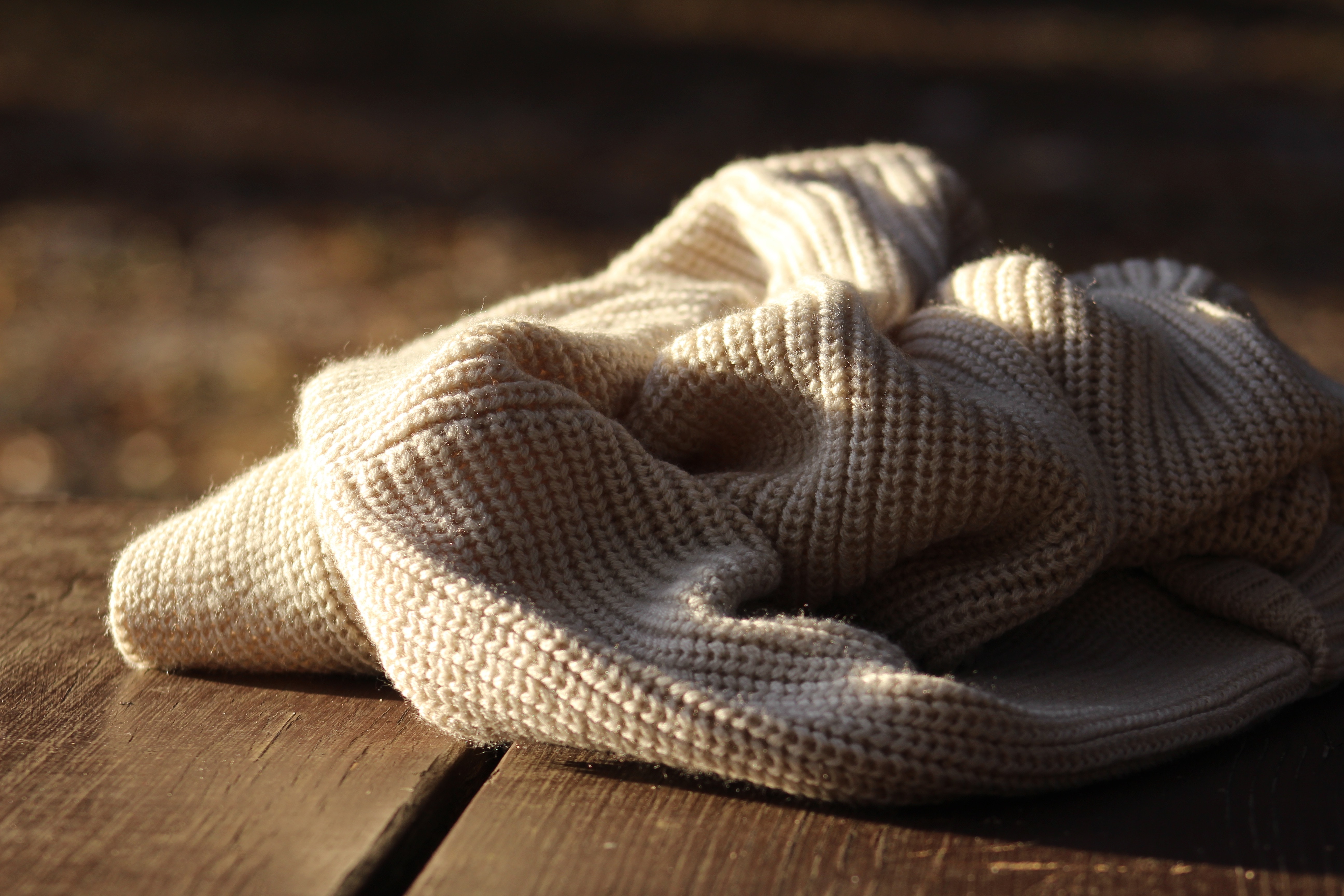 Close-up of a cream-colored cable knit sweater on a wooden surface HD Wallpaper