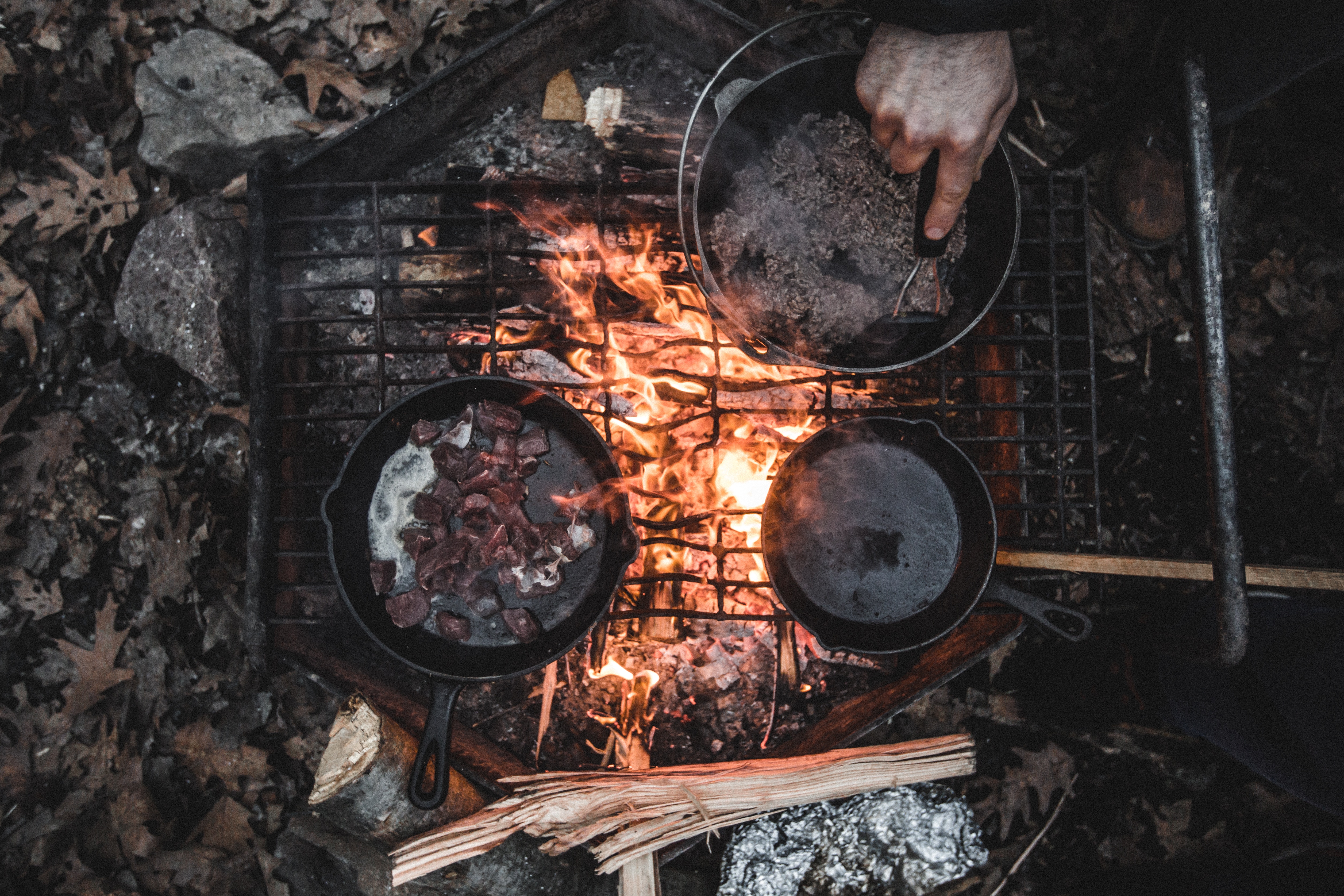 Cooking meat in cast iron pans over a campfire HD Wallpaper