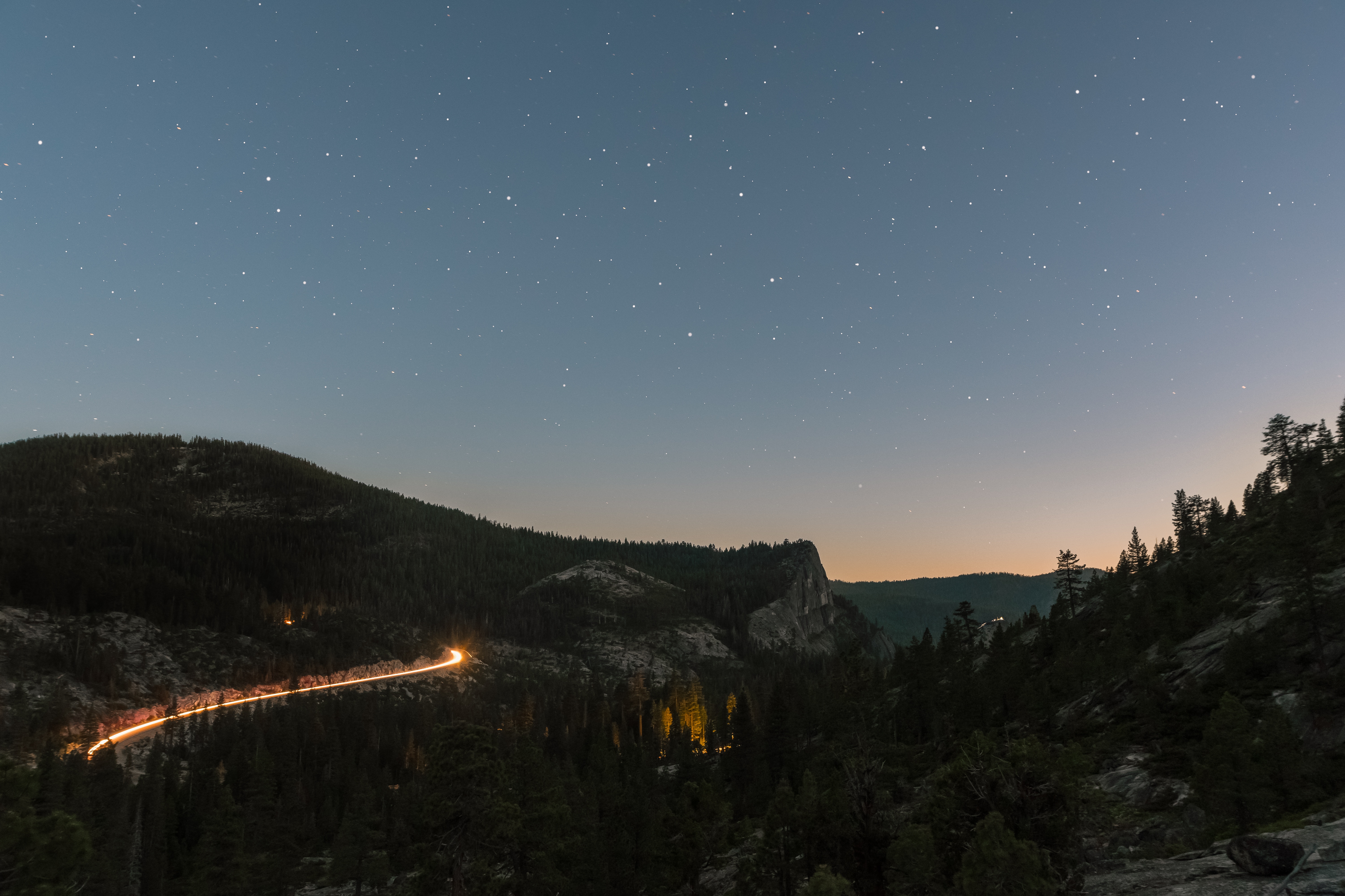 Long exposure of car lights on a mountain road at dusk with stars HD Wallpaper