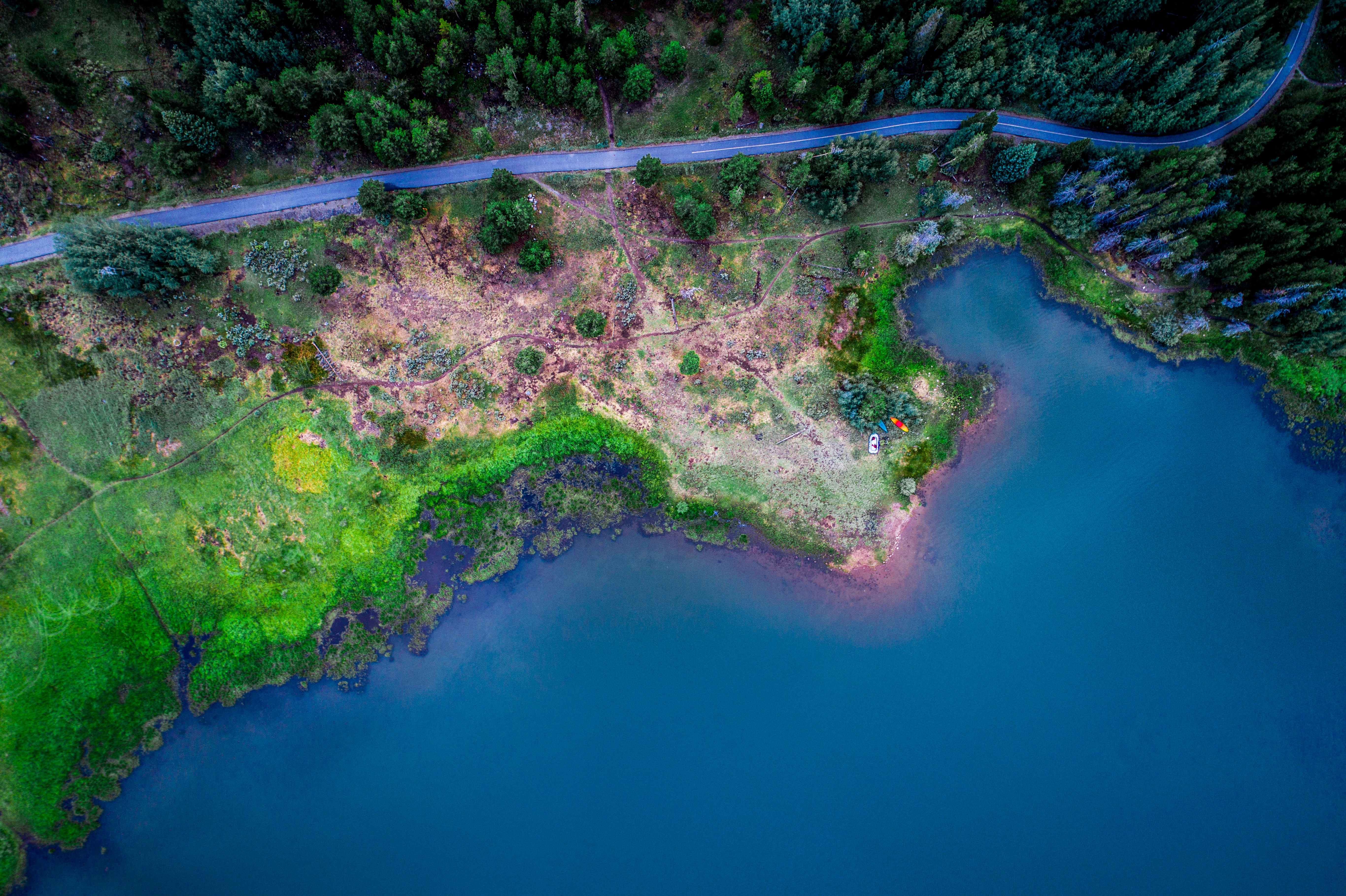 Aerial view of a winding road along a forest and a blue lake HD Wallpaper