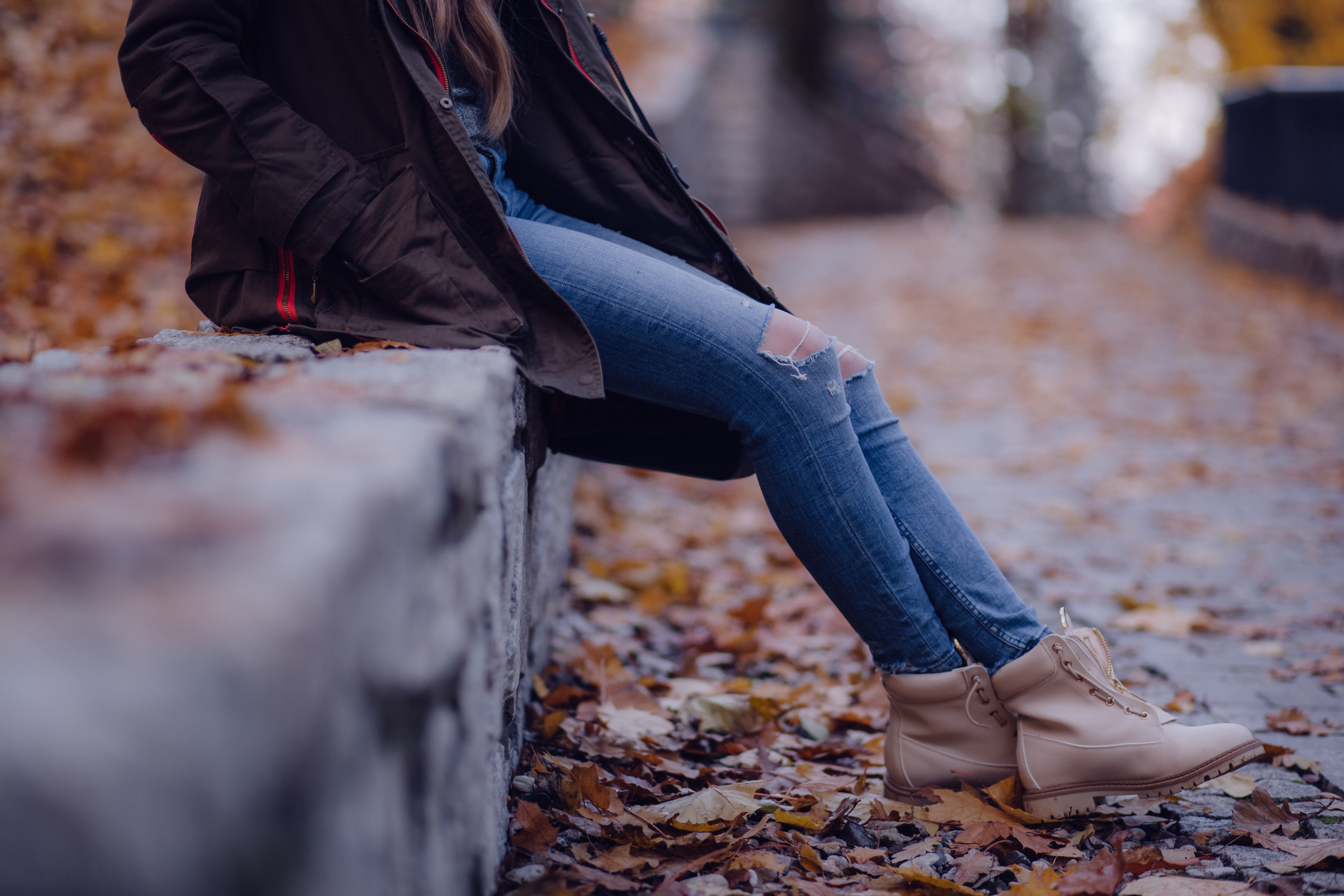 Woman in ripped jeans and boots sitting on a wall in autumn HD Wallpaper