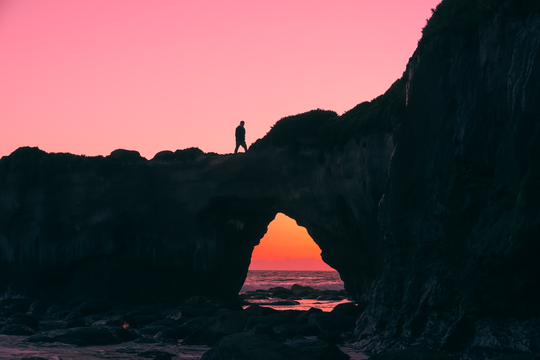 Silhouette of a person walking on a cliff overlooking the ocean at sunset HD Wallpaper