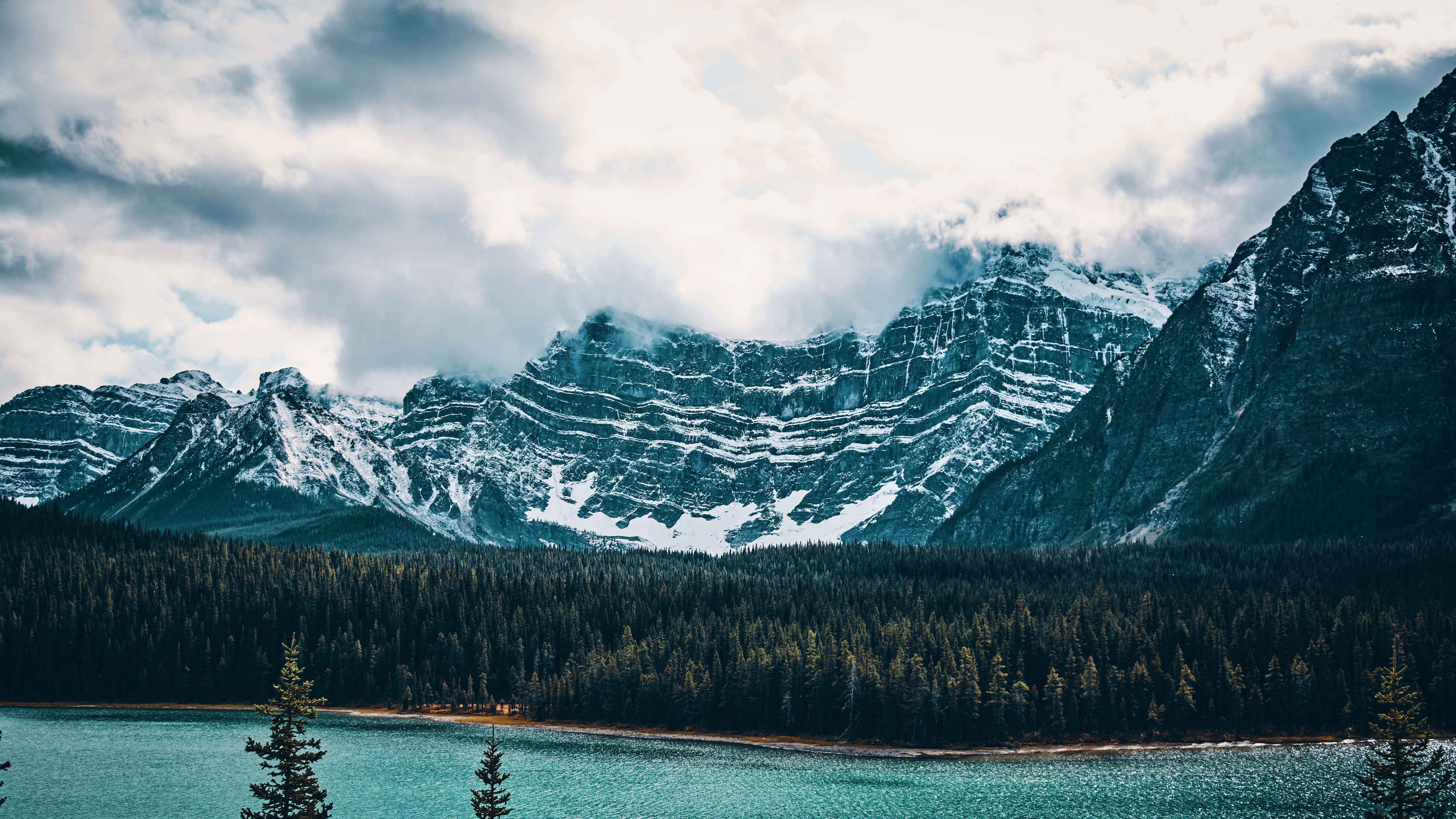 Snow-capped mountains over a teal lake and forest HD Wallpaper