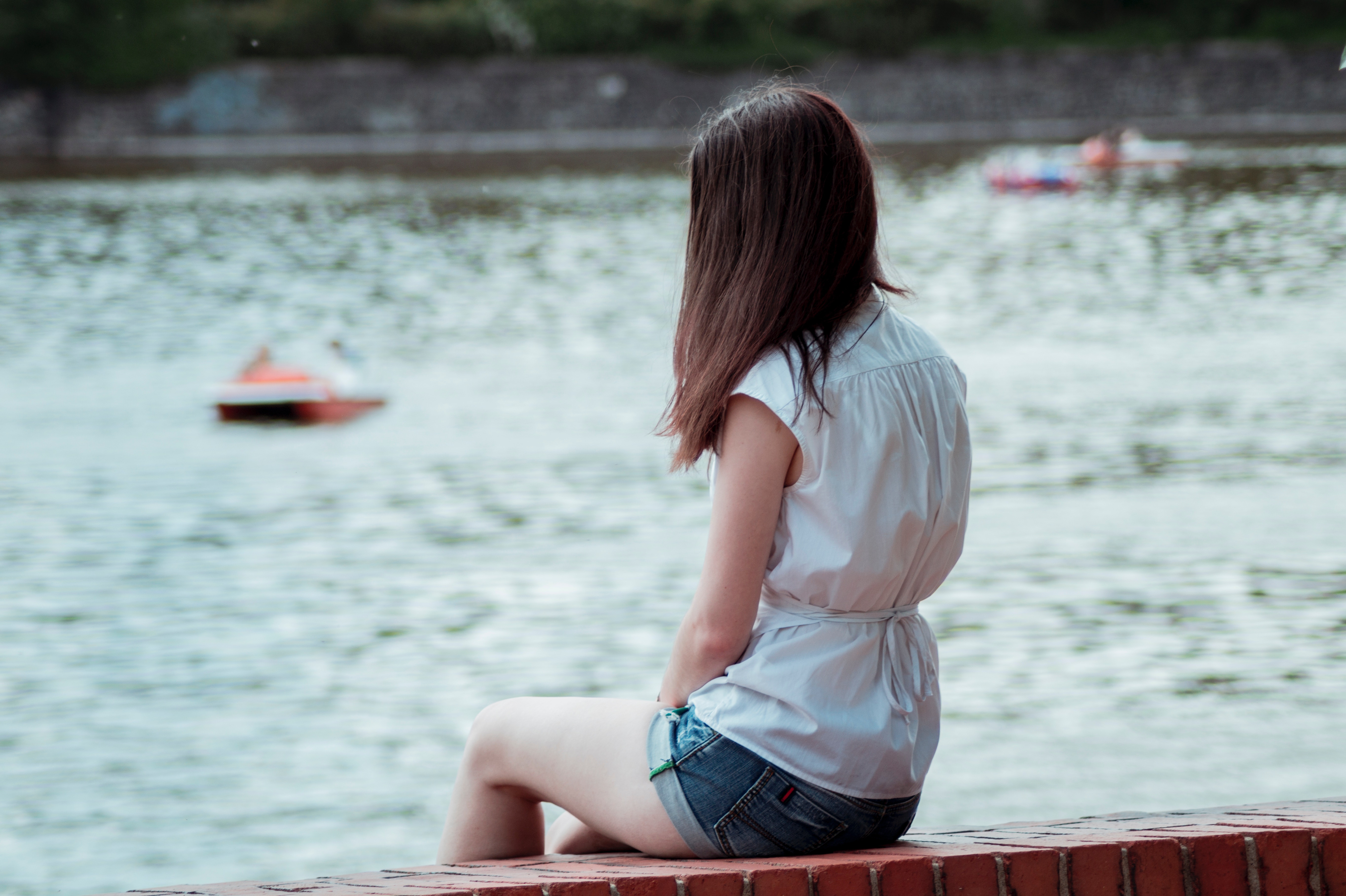 Woman sitting by a lake with boats HD Wallpaper