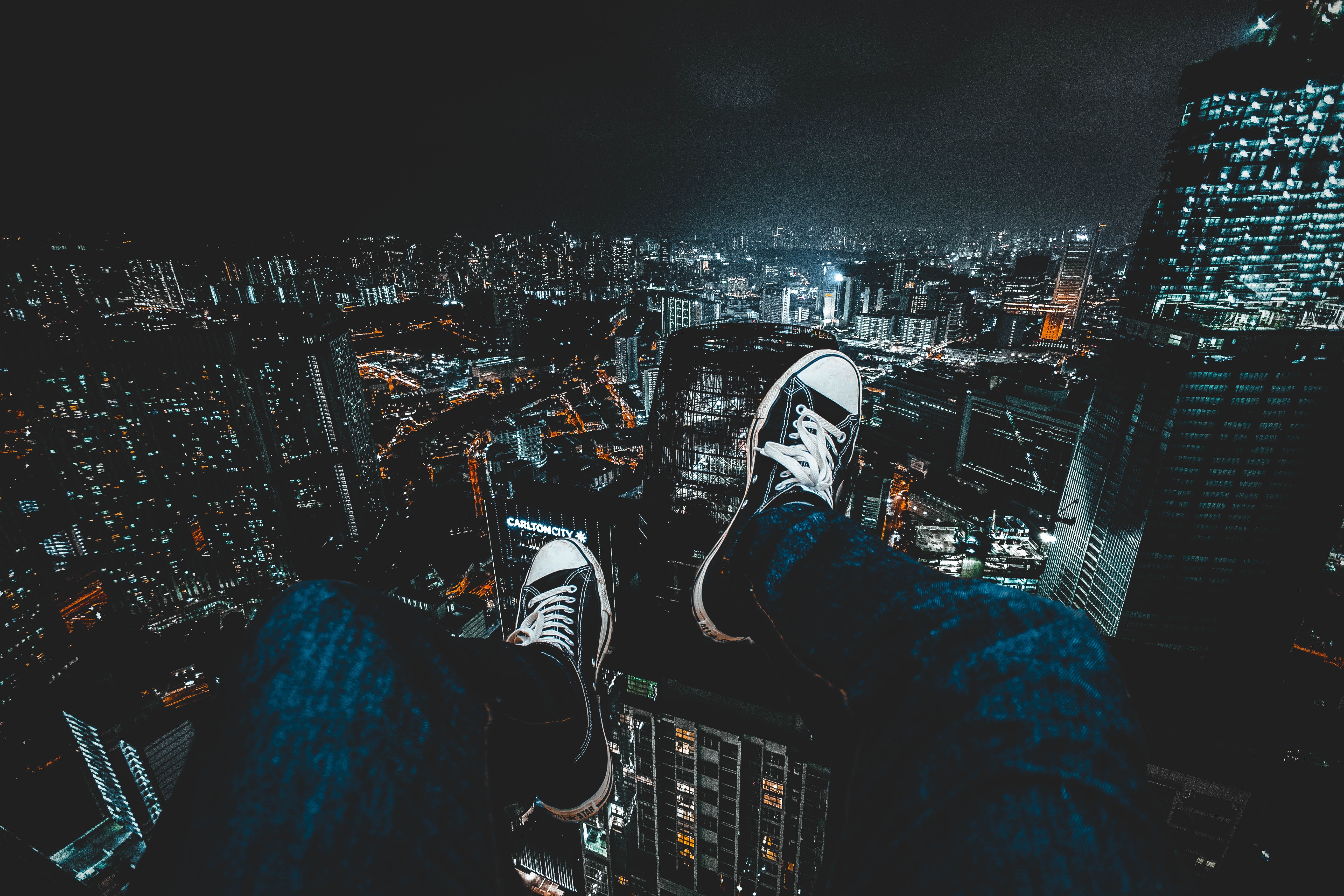 Person sitting on a skyscraper overlooking a city at night HD Wallpaper