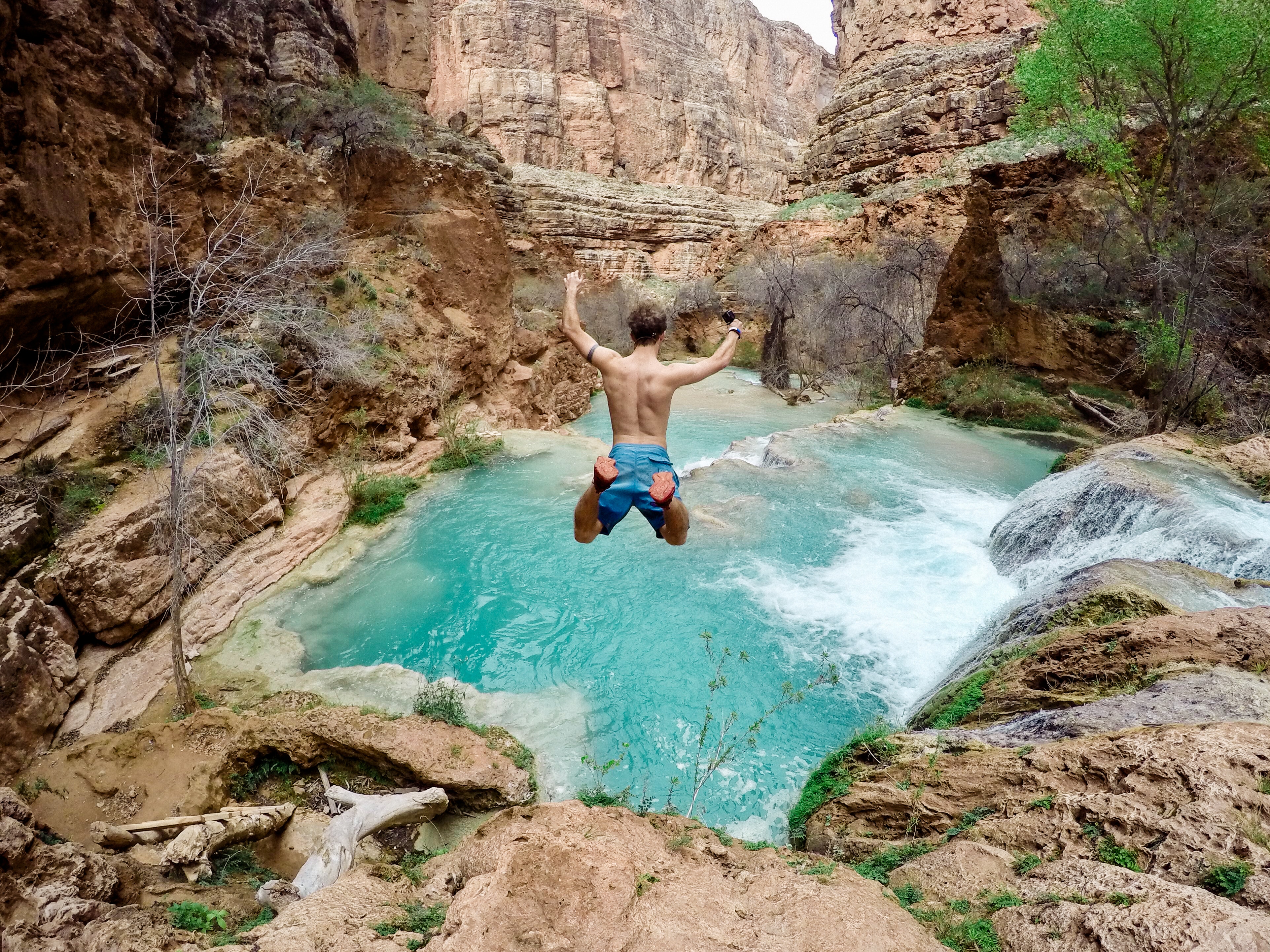 Man jumping into a turquoise waterfall pool HD Wallpaper