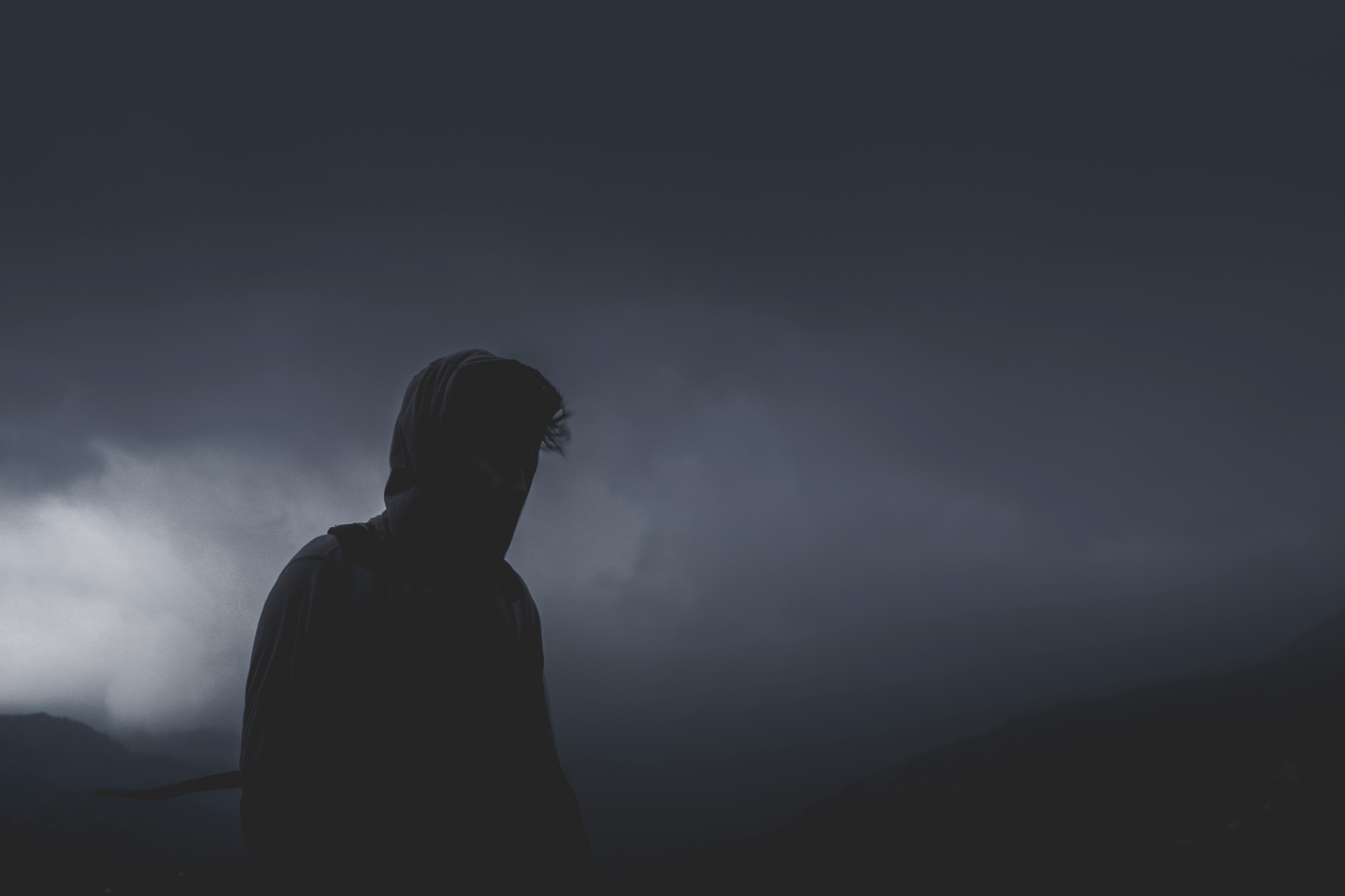 Person in hoodie against dark cloudy sky HD Wallpaper