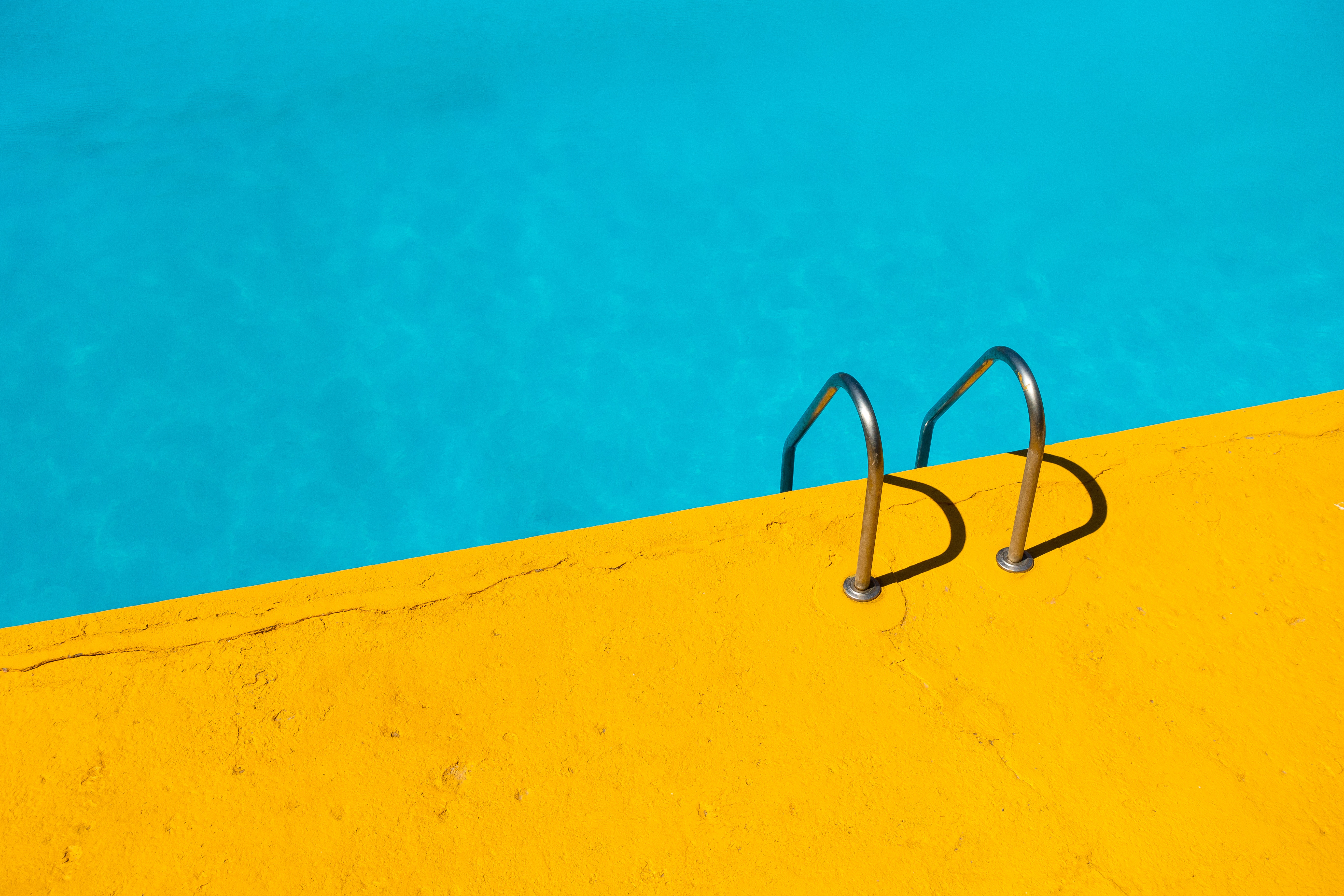 Yellow poolside with blue swimming pool and handrails HD Wallpaper