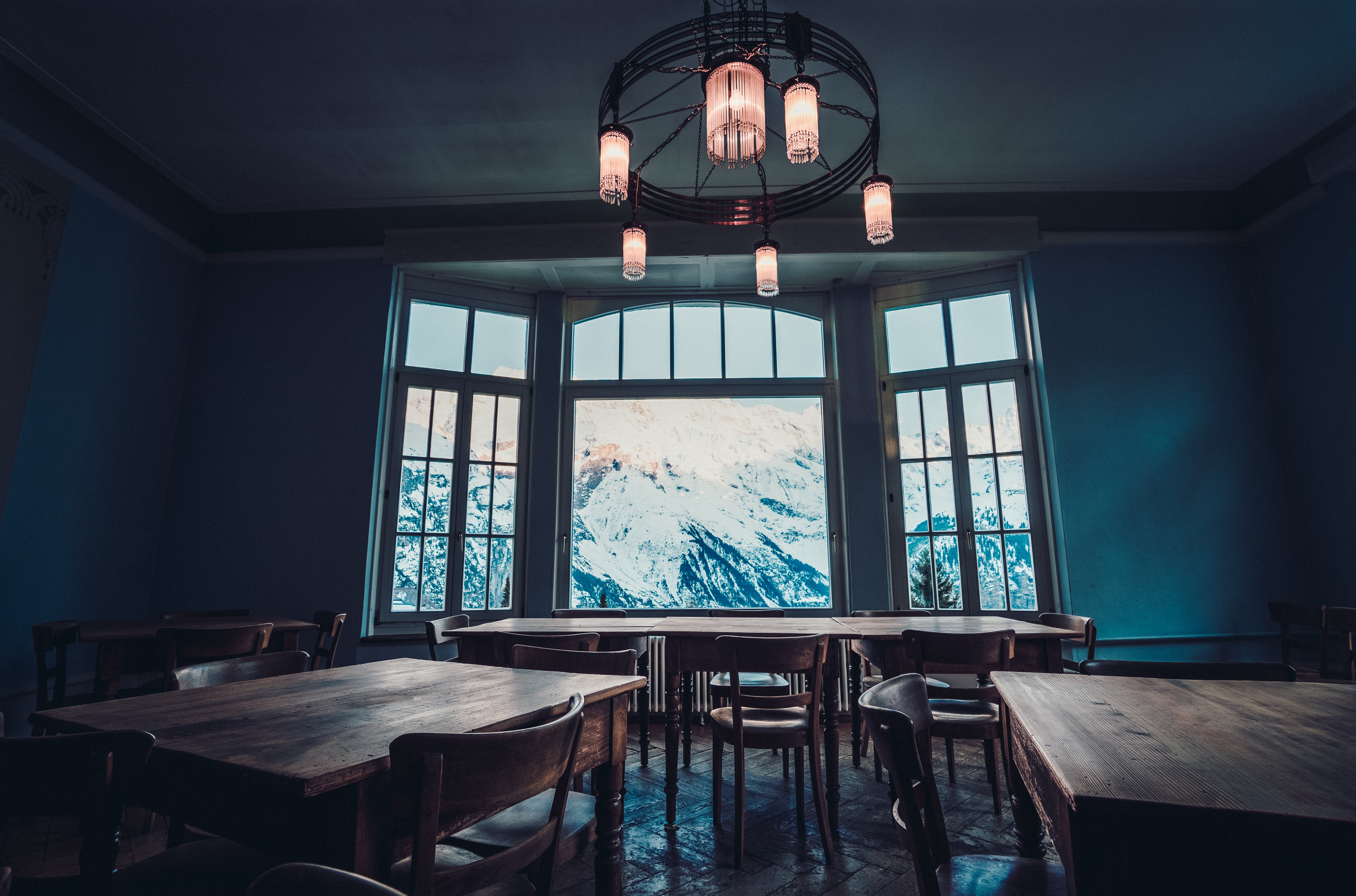 Interior of a room with tables and chairs overlooking a snowy mountain range HD Wallpaper