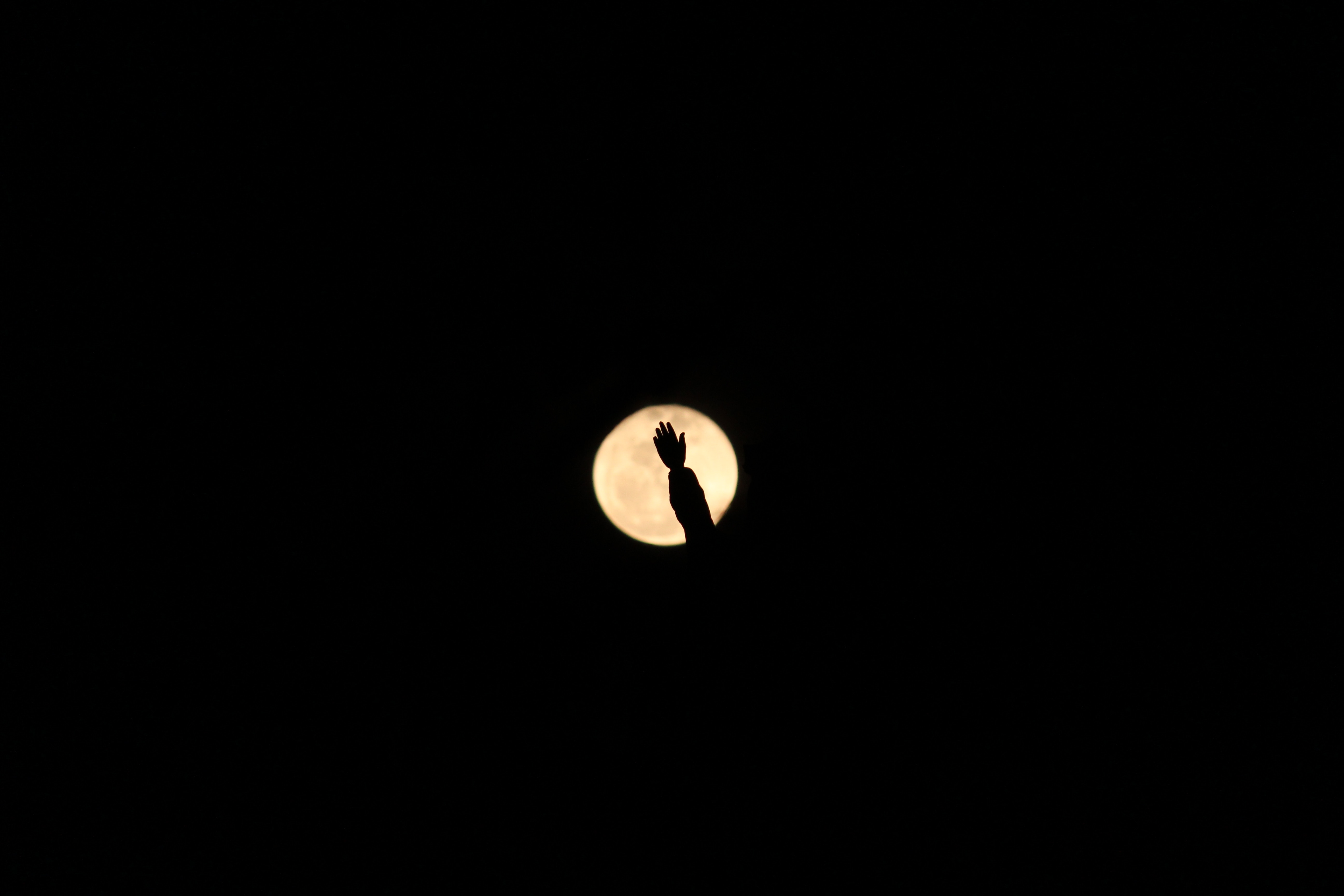 Silhouette of a hand waving in front of the moon HD Wallpaper