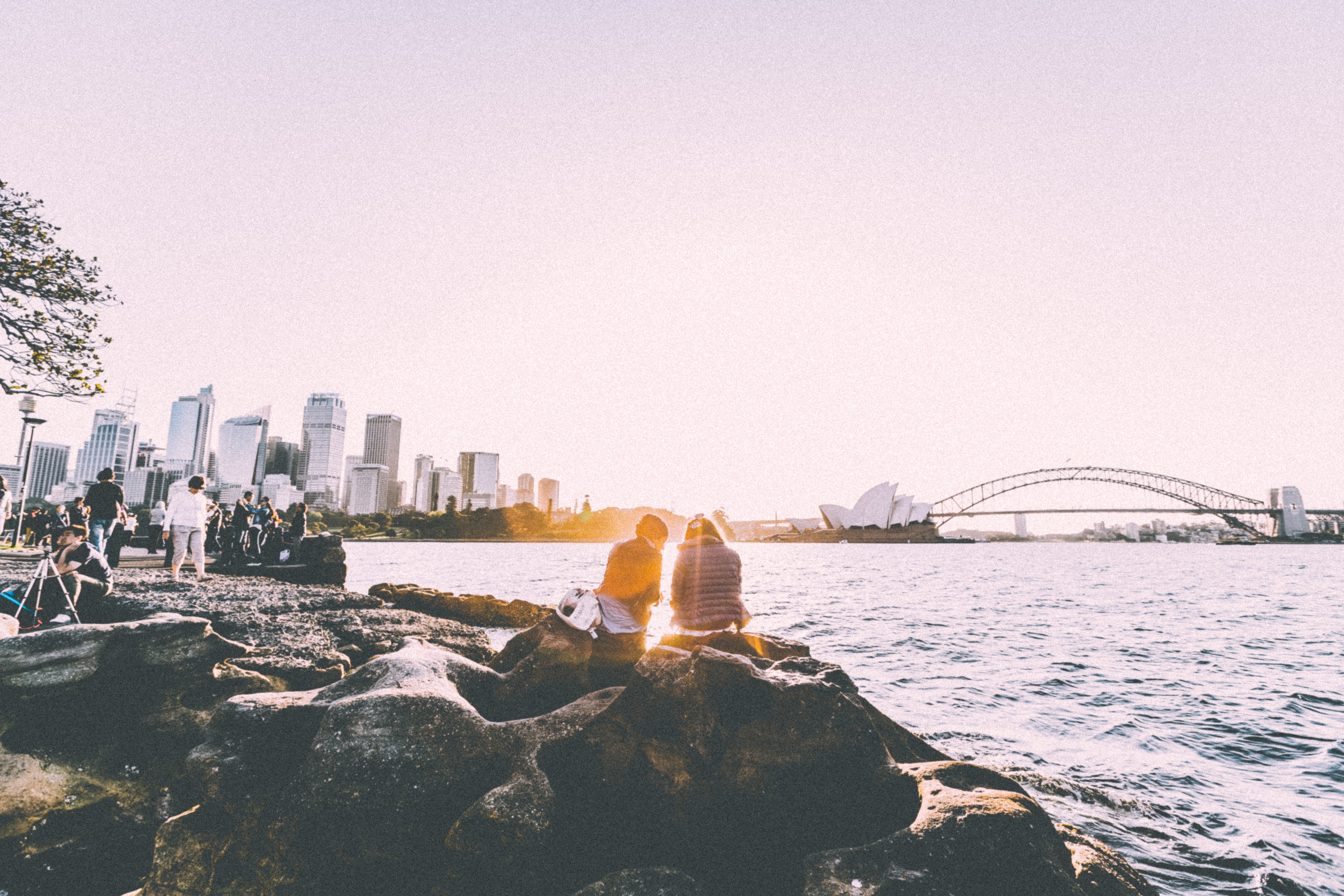 Couple sitting on rocks overlooking Sydney Harbour at sunset HD Wallpaper