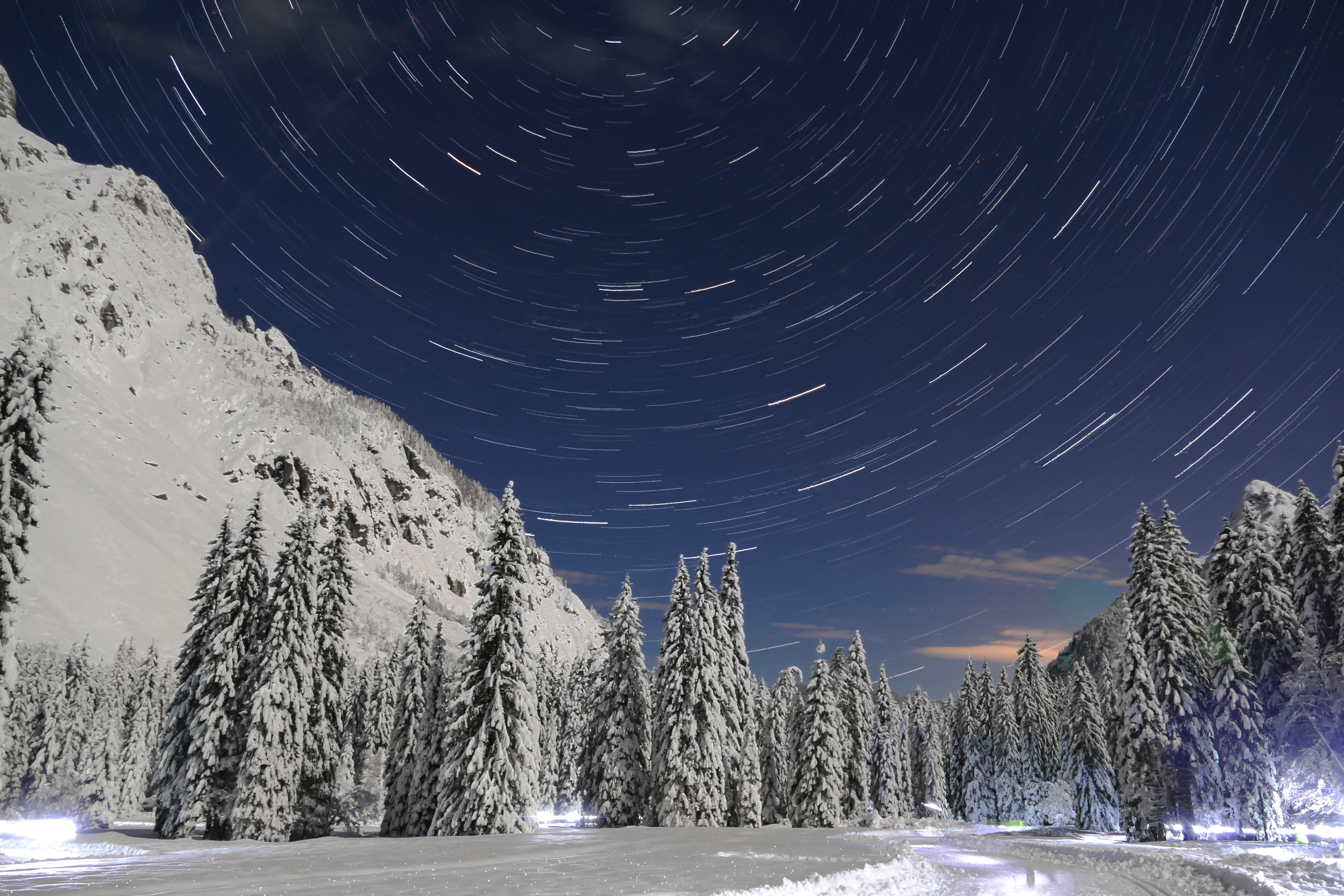 Star trails over a snowy mountain forest at night HD Wallpaper
