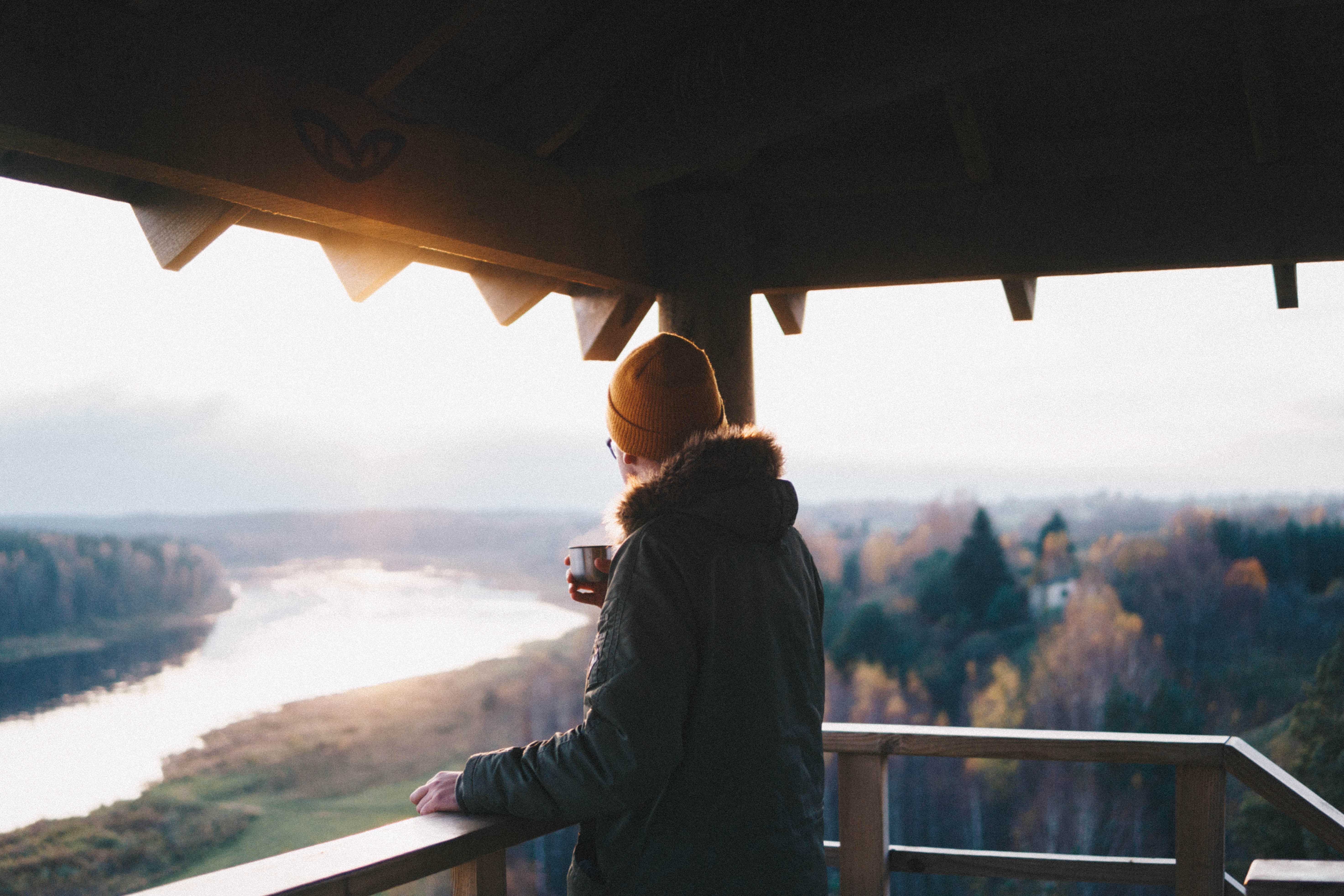 Person holding a cup on a balcony overlooking a river in autumn HD Wallpaper