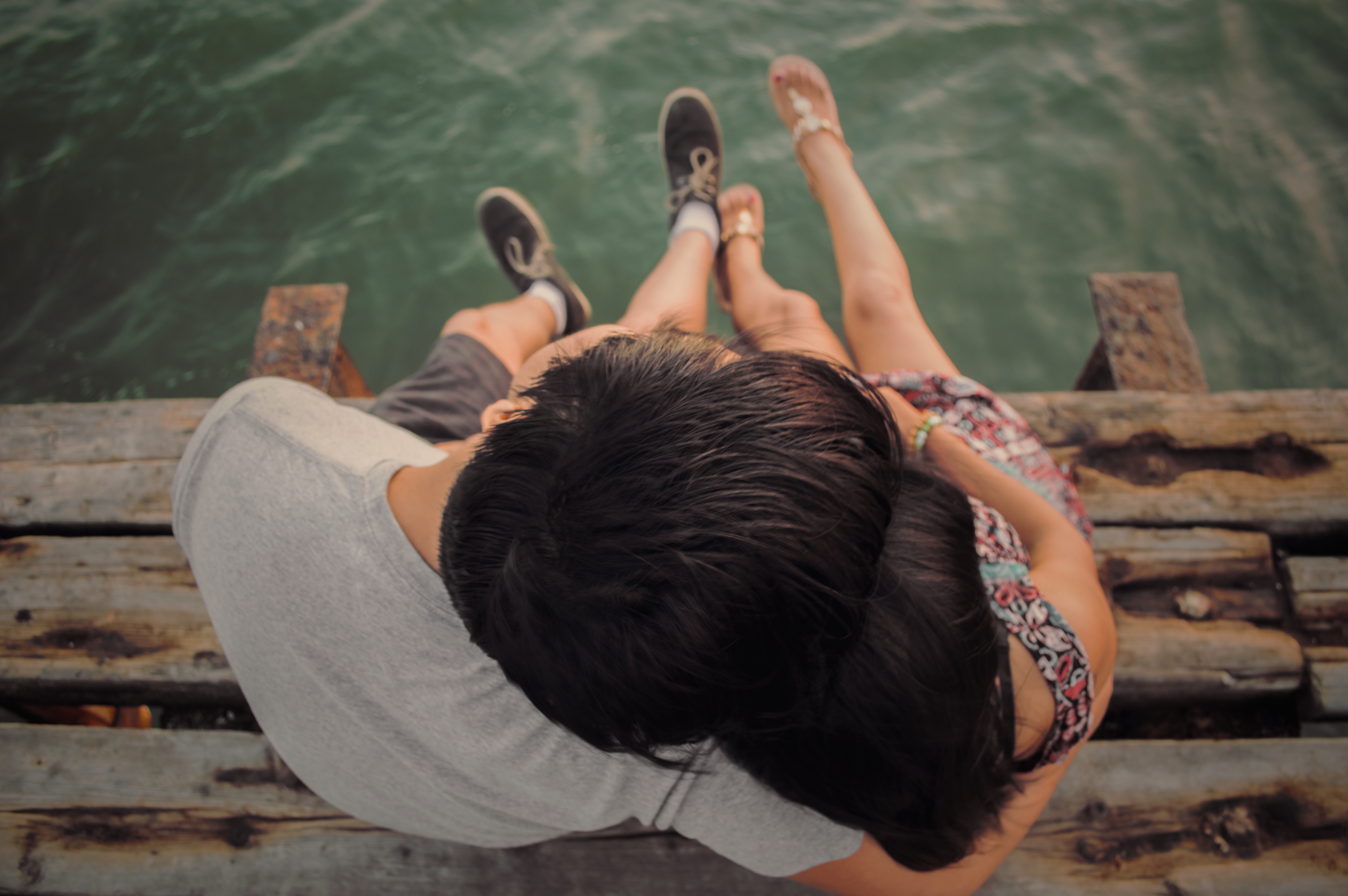 Couple sitting on a dock by the water HD Wallpaper