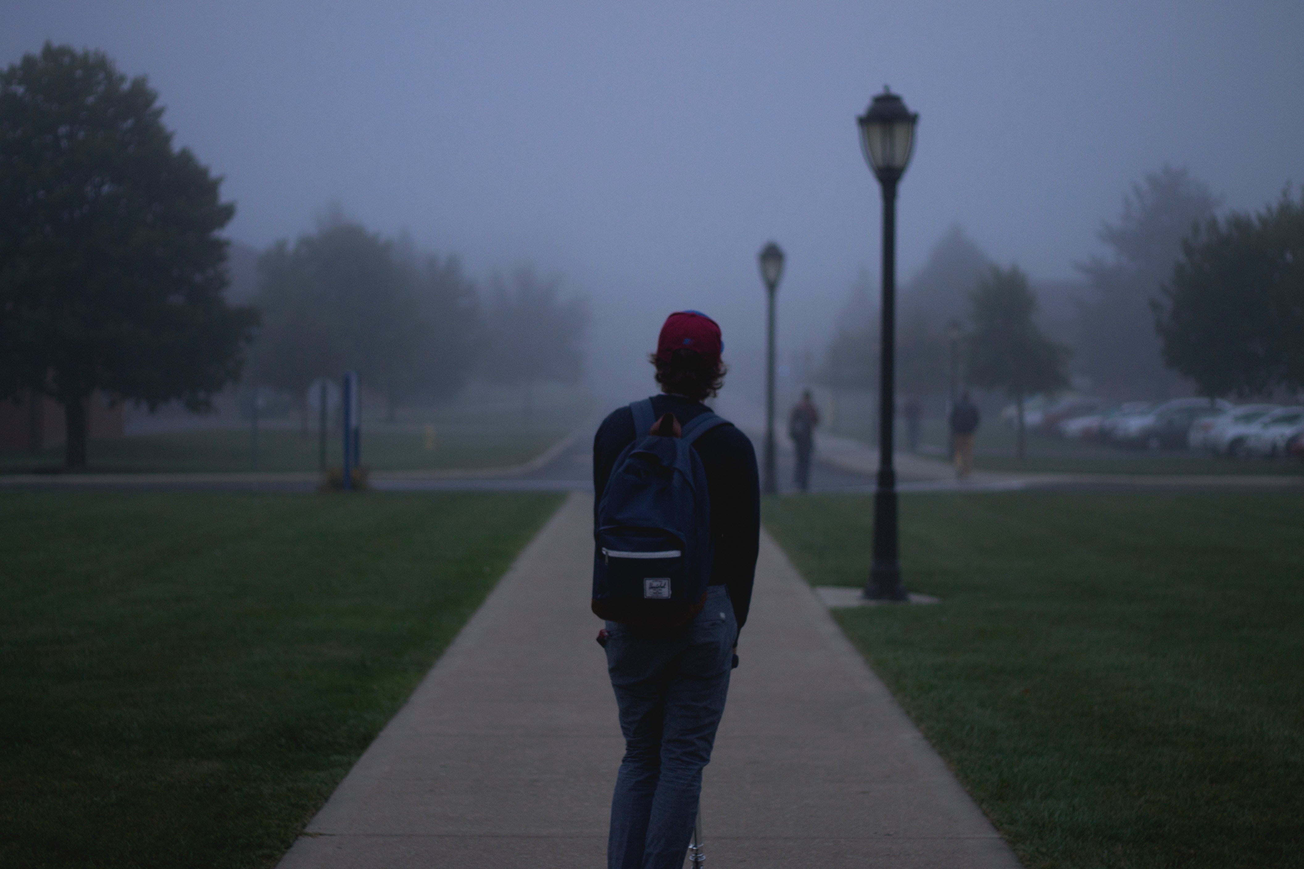 Student with backpack walking on foggy campus path HD Wallpaper