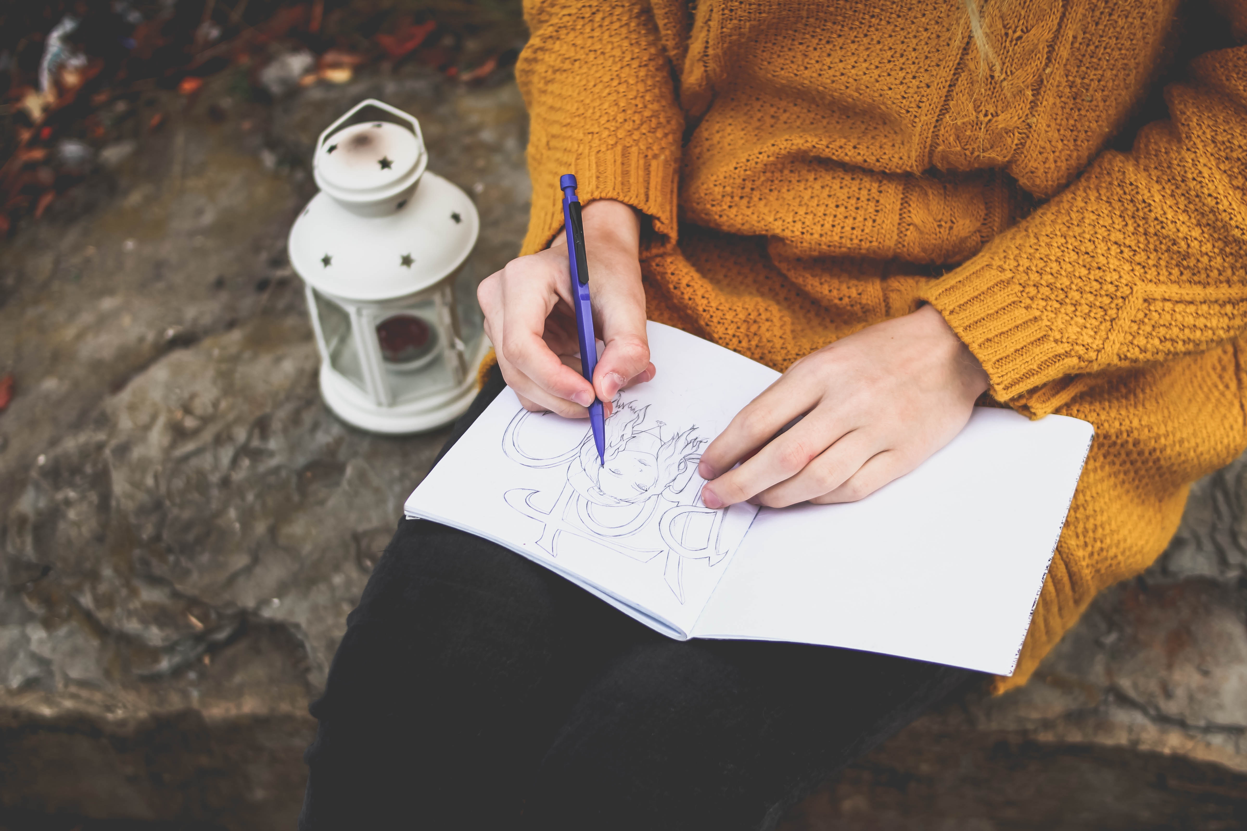 Woman drawing in a notebook next to a lantern HD Wallpaper
