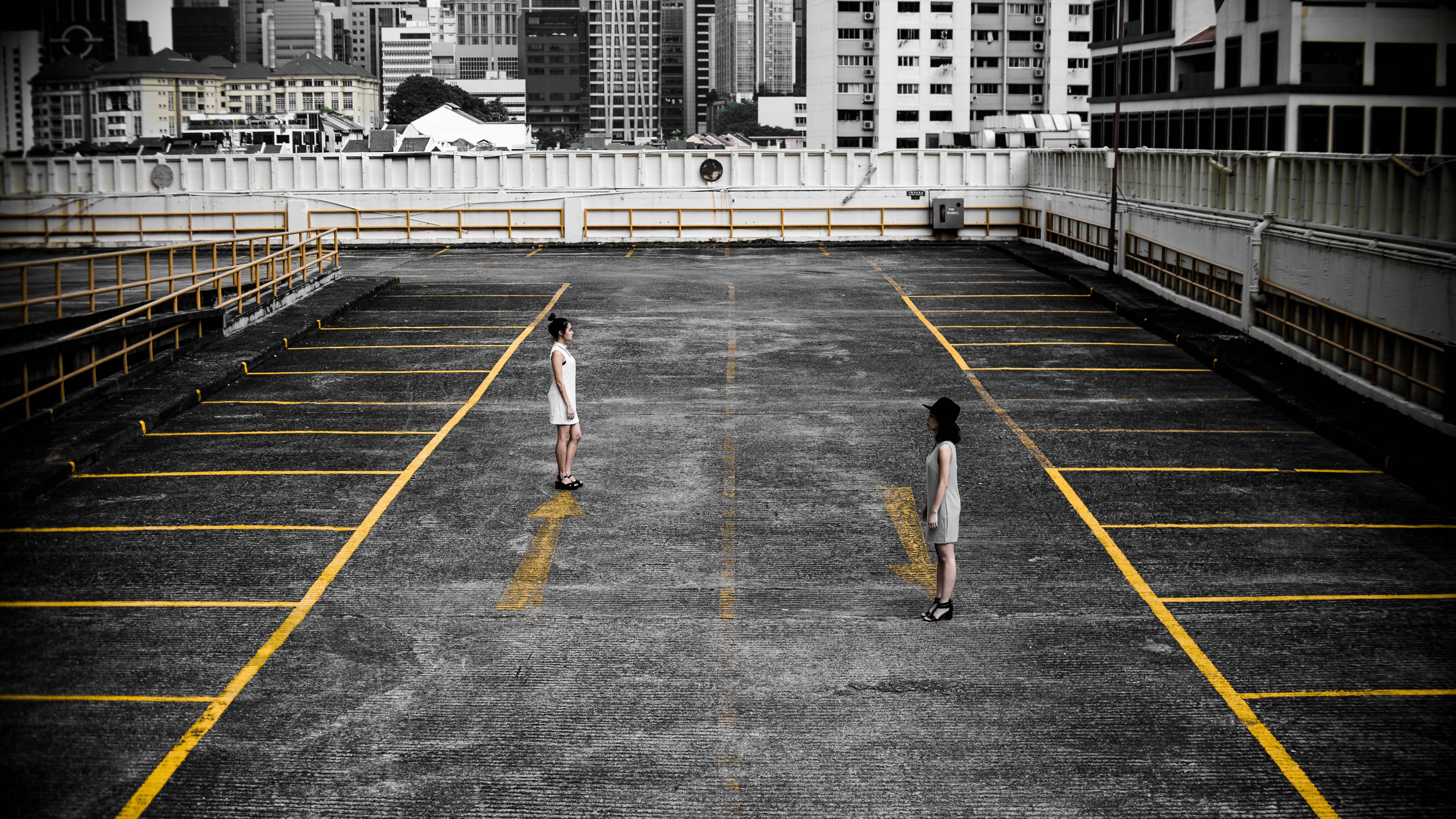 Two women standing in a desaturated parking lot HD Wallpaper