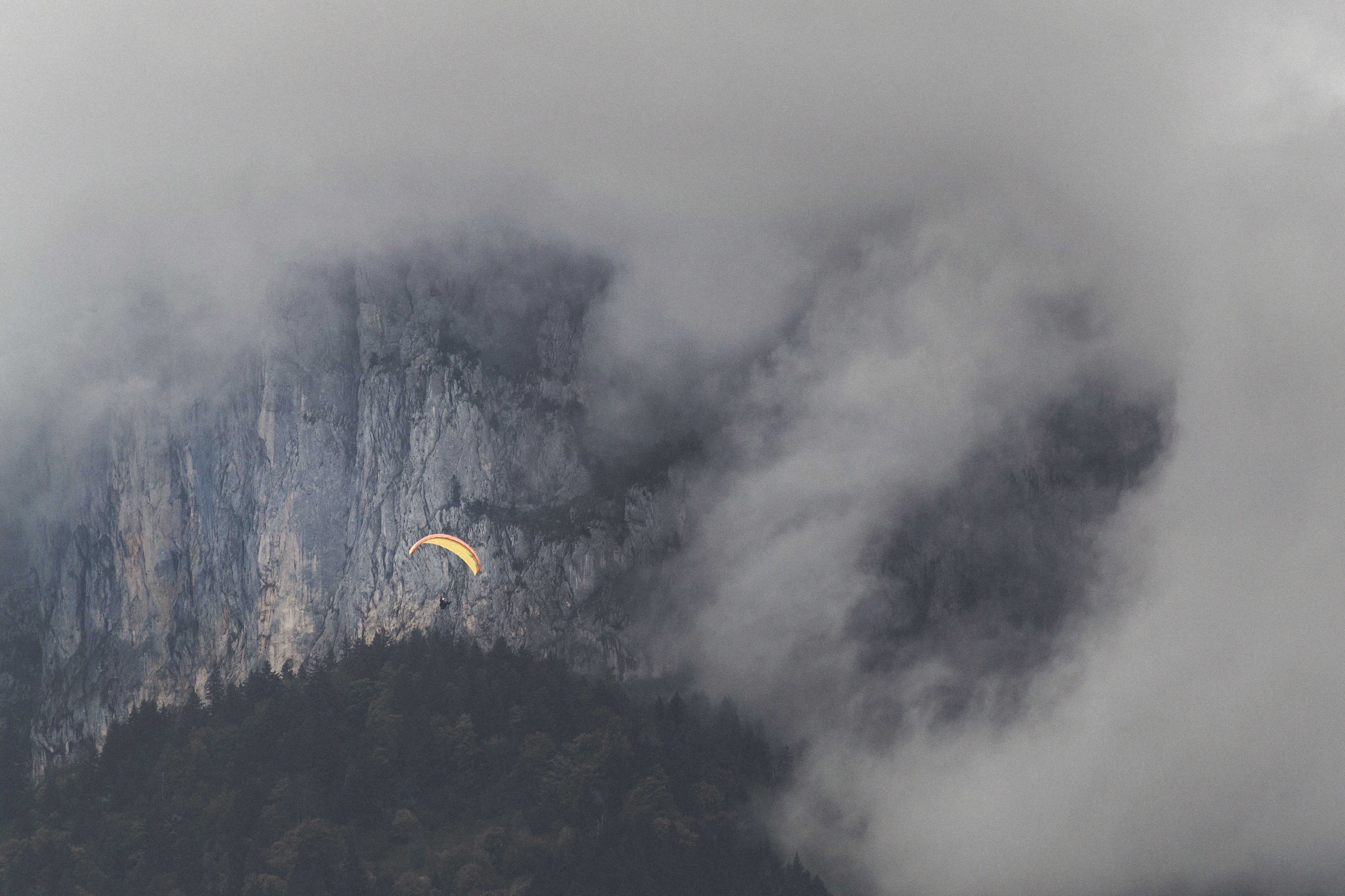 Paraglider flying near a foggy mountain cliff HD Wallpaper