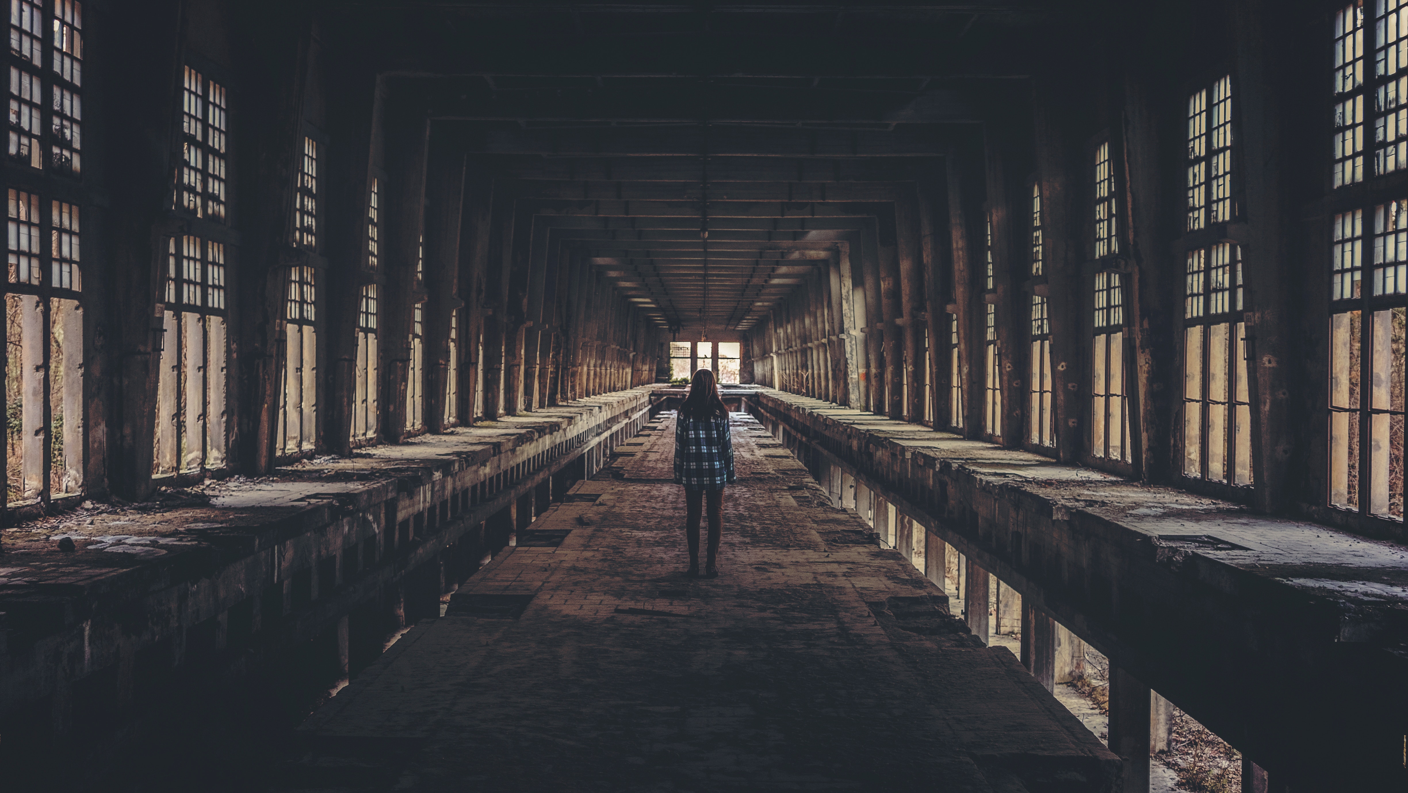 Woman standing in a long, abandoned corridor with windows HD Wallpaper