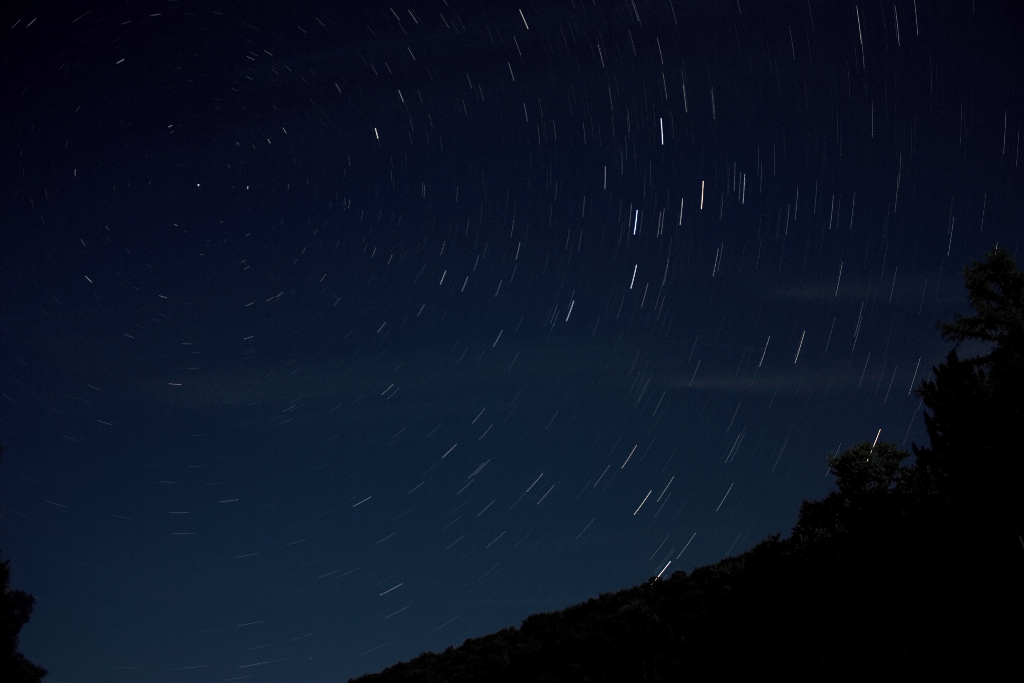 Star trails in the night sky over a silhouetted landscape HD Wallpaper