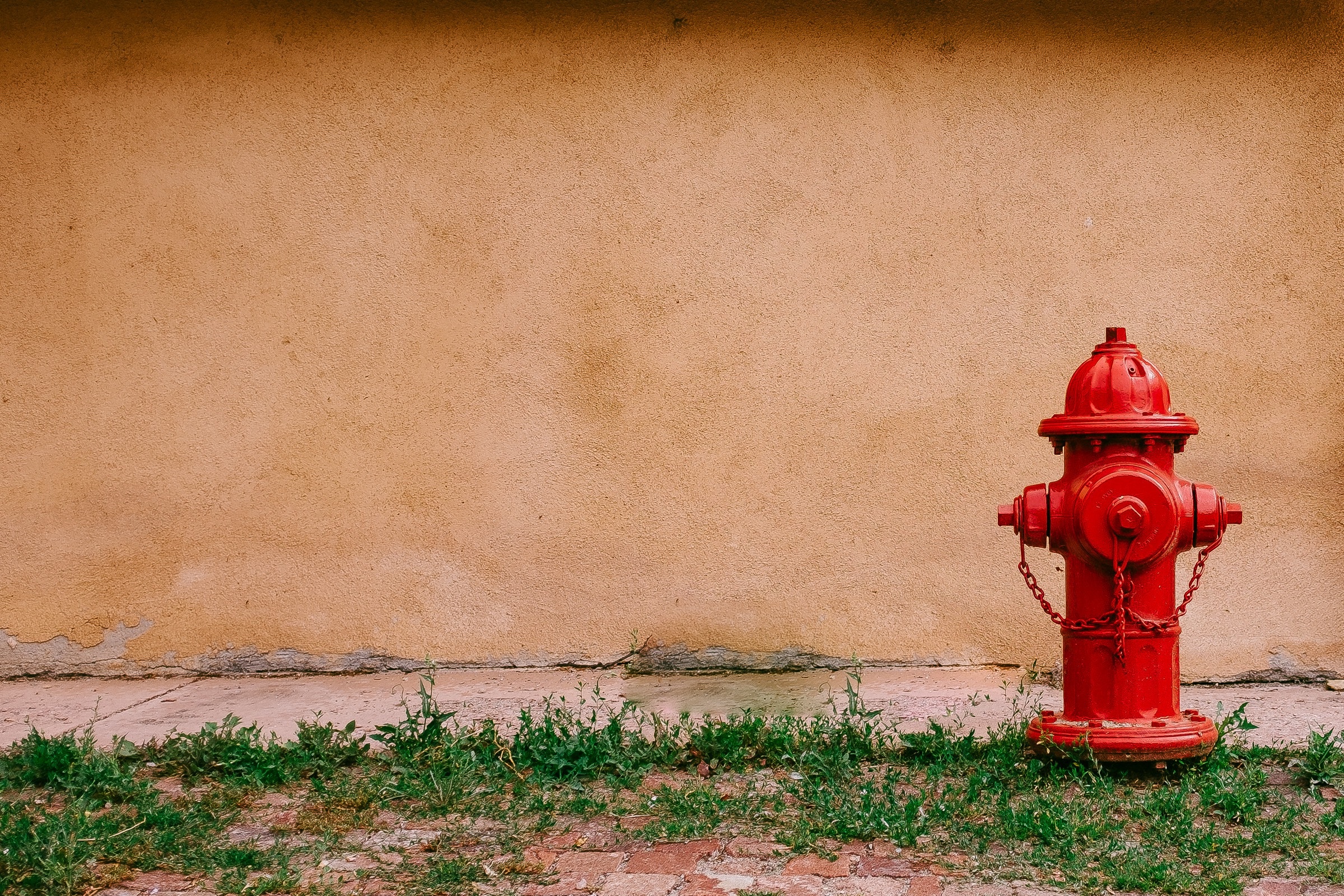 Red fire hydrant against a tan wall HD Wallpaper