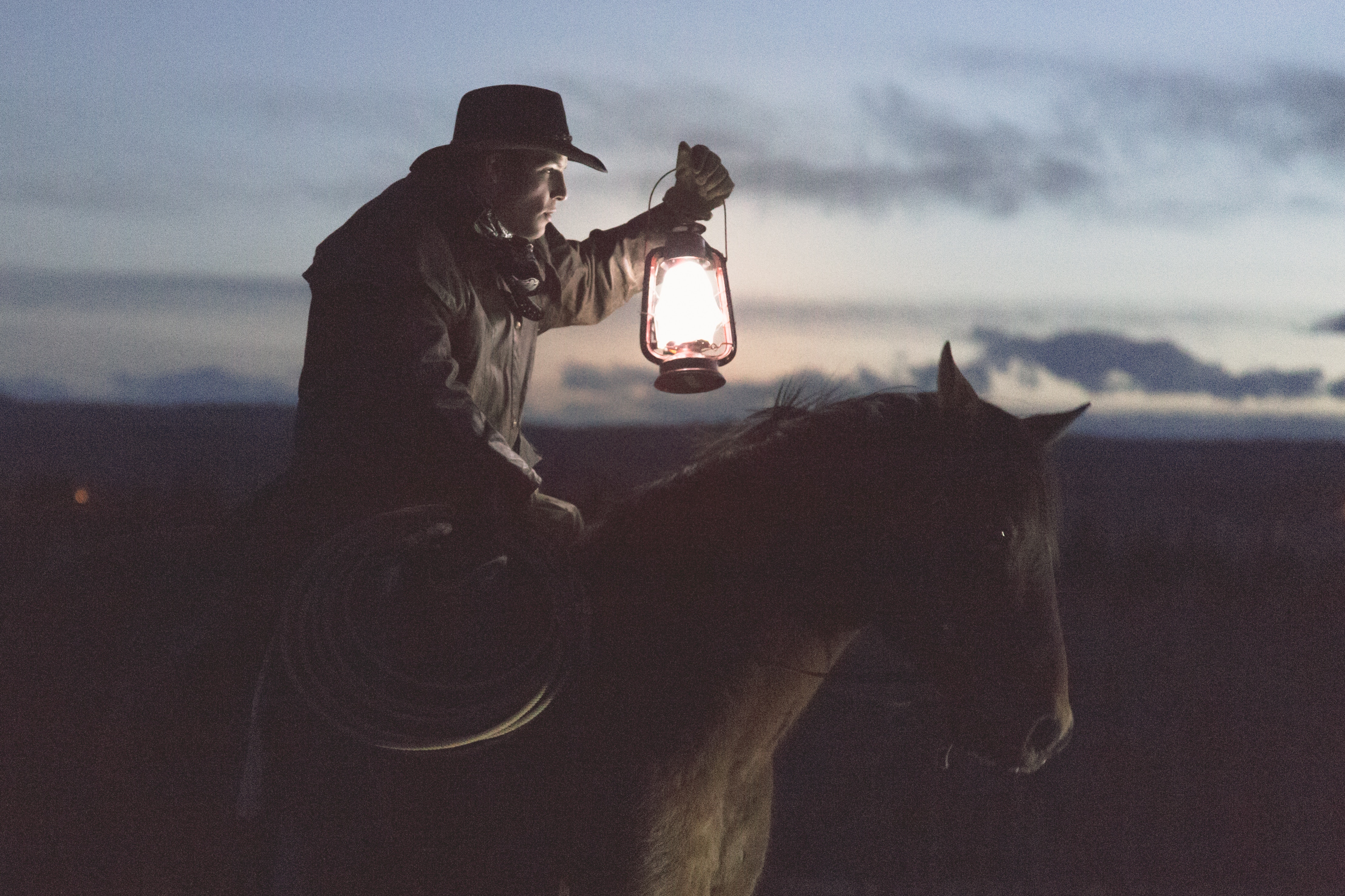 Cowboy riding a horse at dusk with a lantern HD Wallpaper