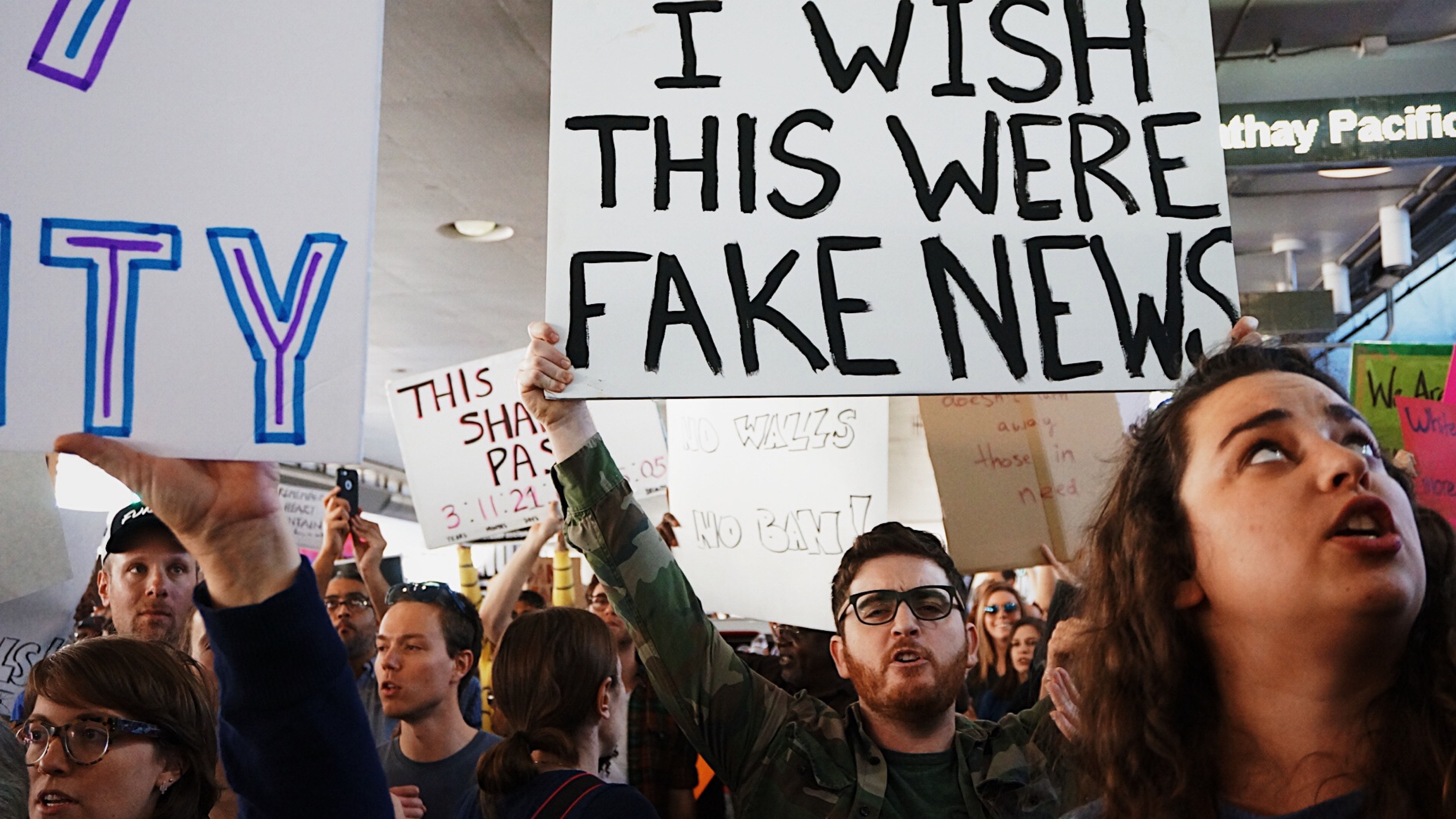 Protesters hold signs including "I WISH THIS WERE FAKE NEWS" HD Wallpaper