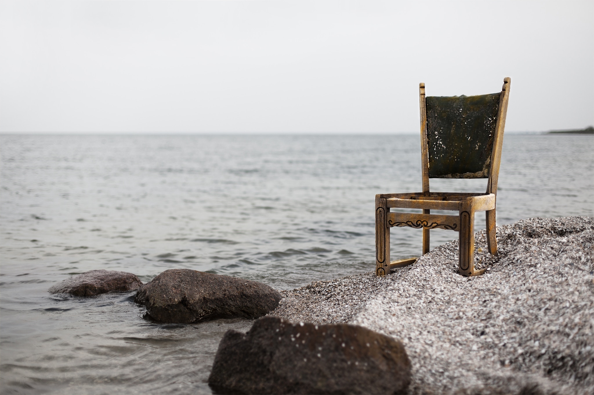 An old chair sits on a rocky shore by the sea HD Wallpaper