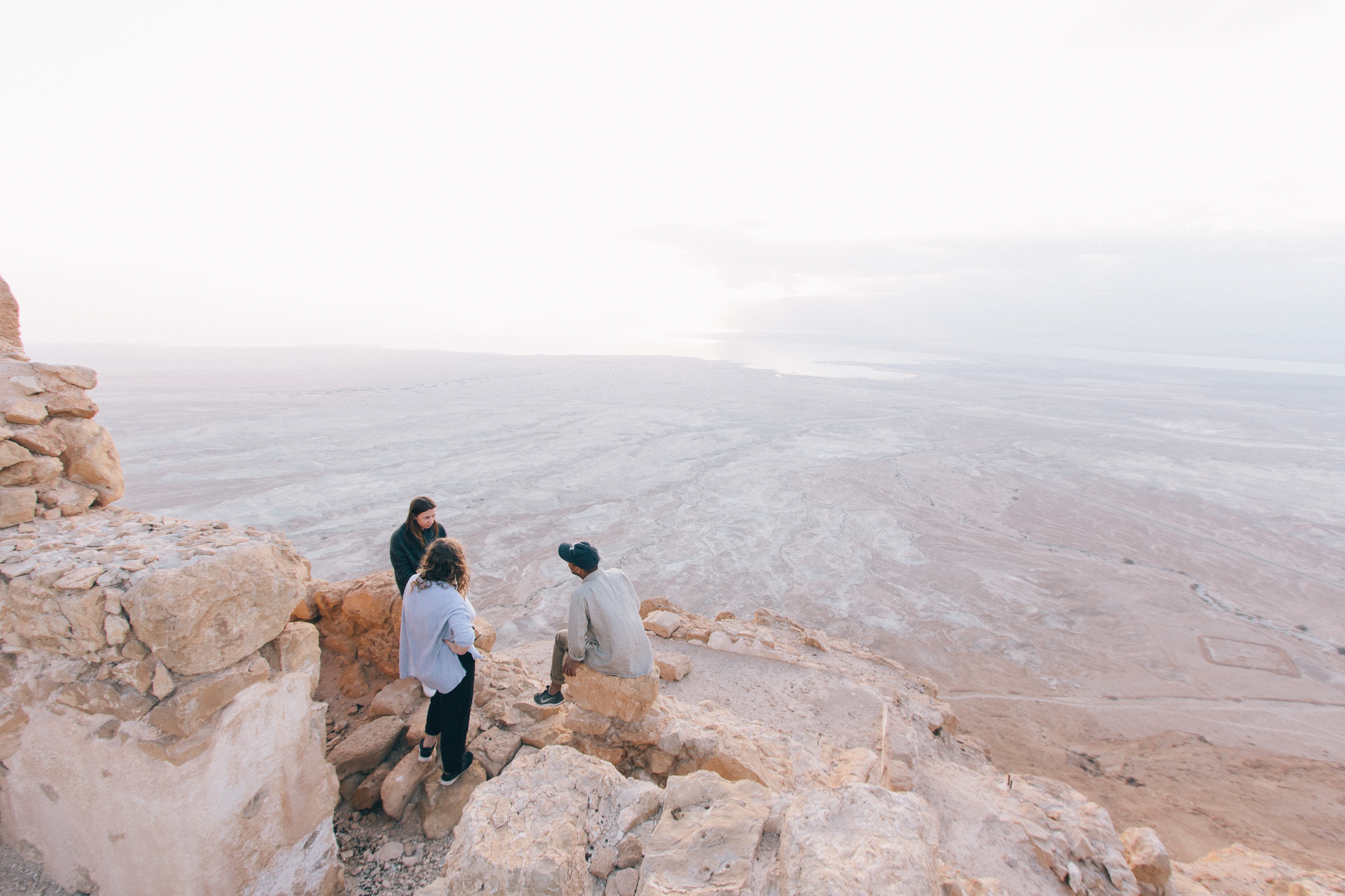 People on a rocky cliff overlooking a desert landscape HD Wallpaper