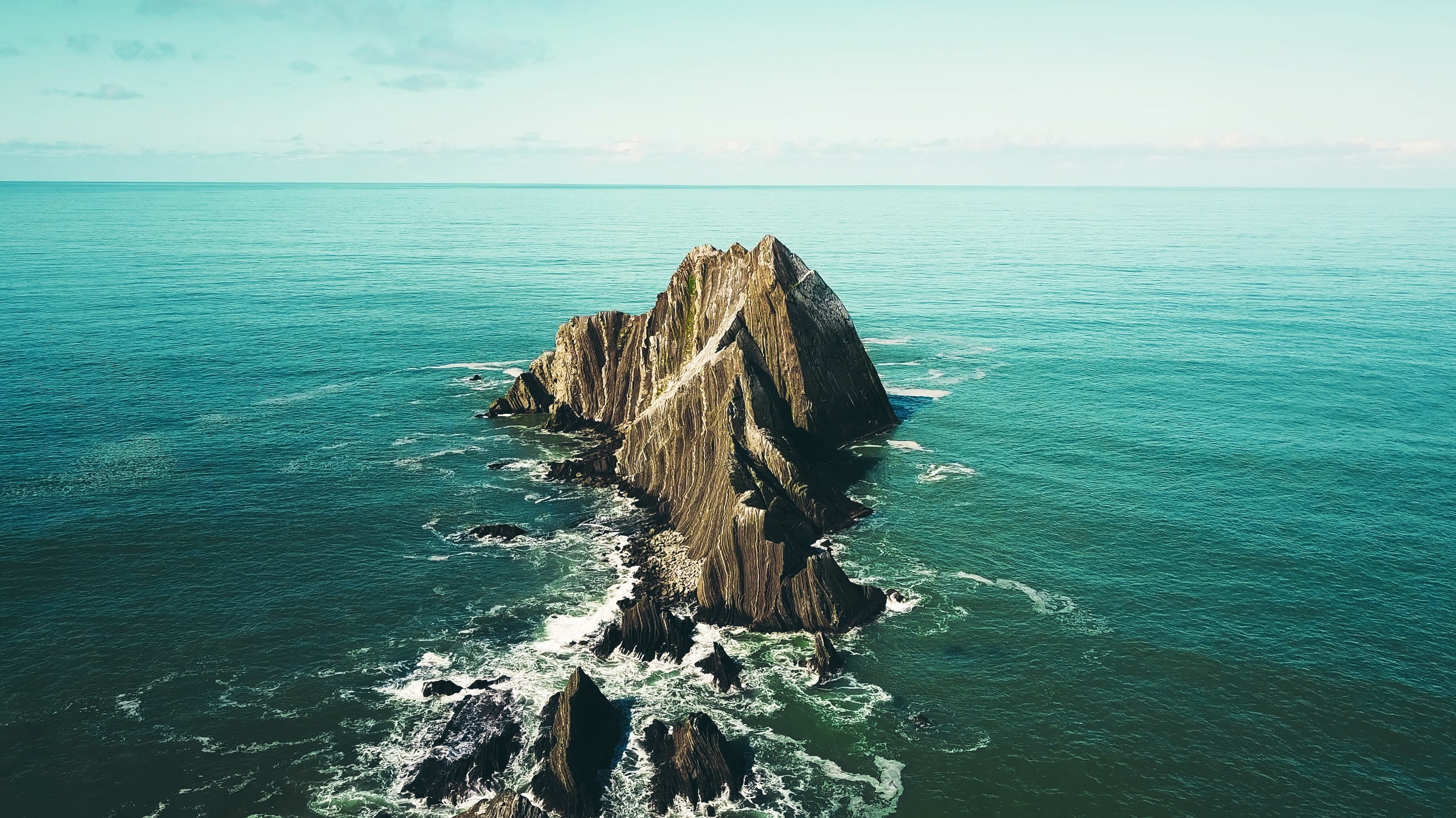 Jagged rock formation in the ocean under a clear sky HD Wallpaper