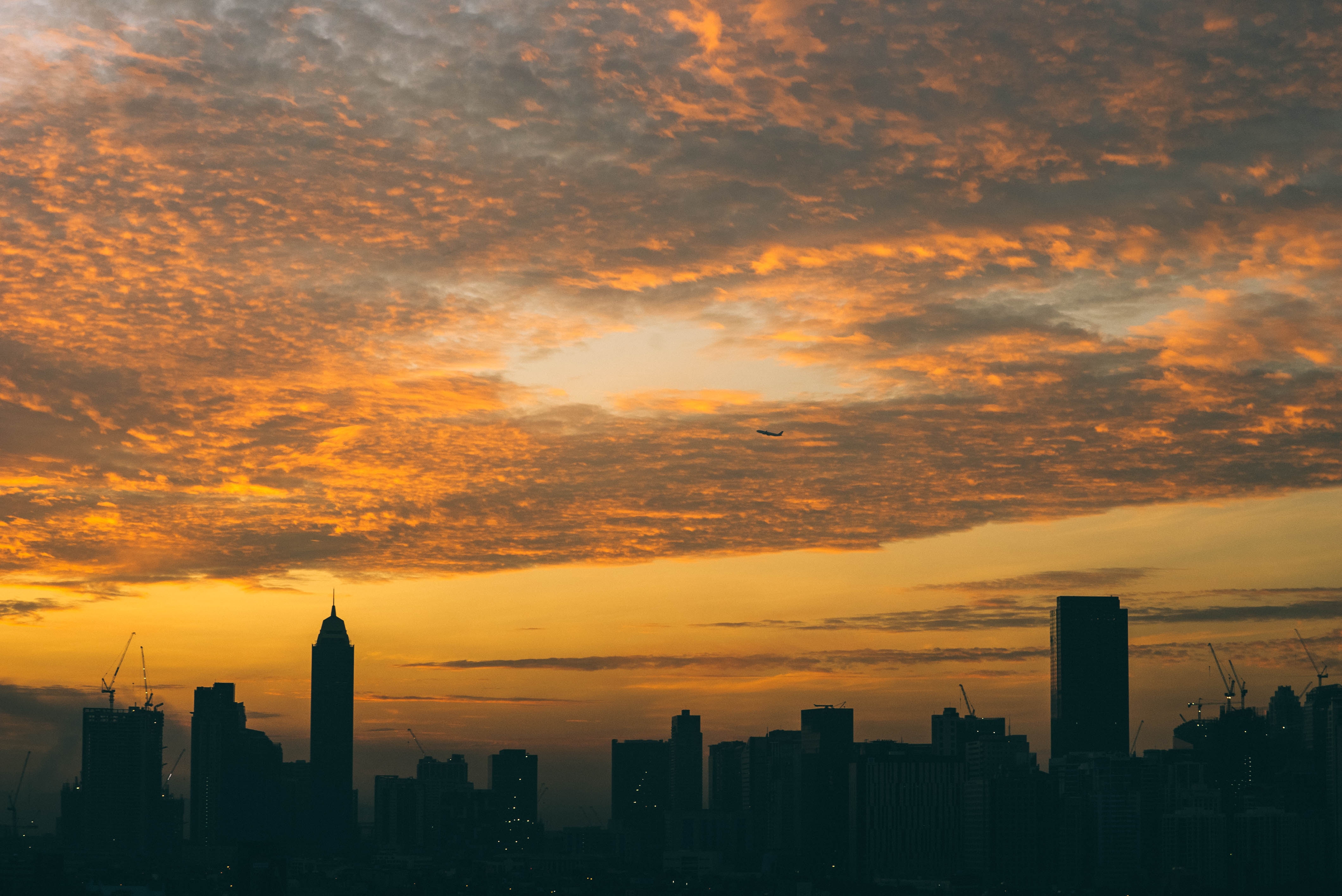 City skyline at sunrise with airplane in orange clouds HD Wallpaper