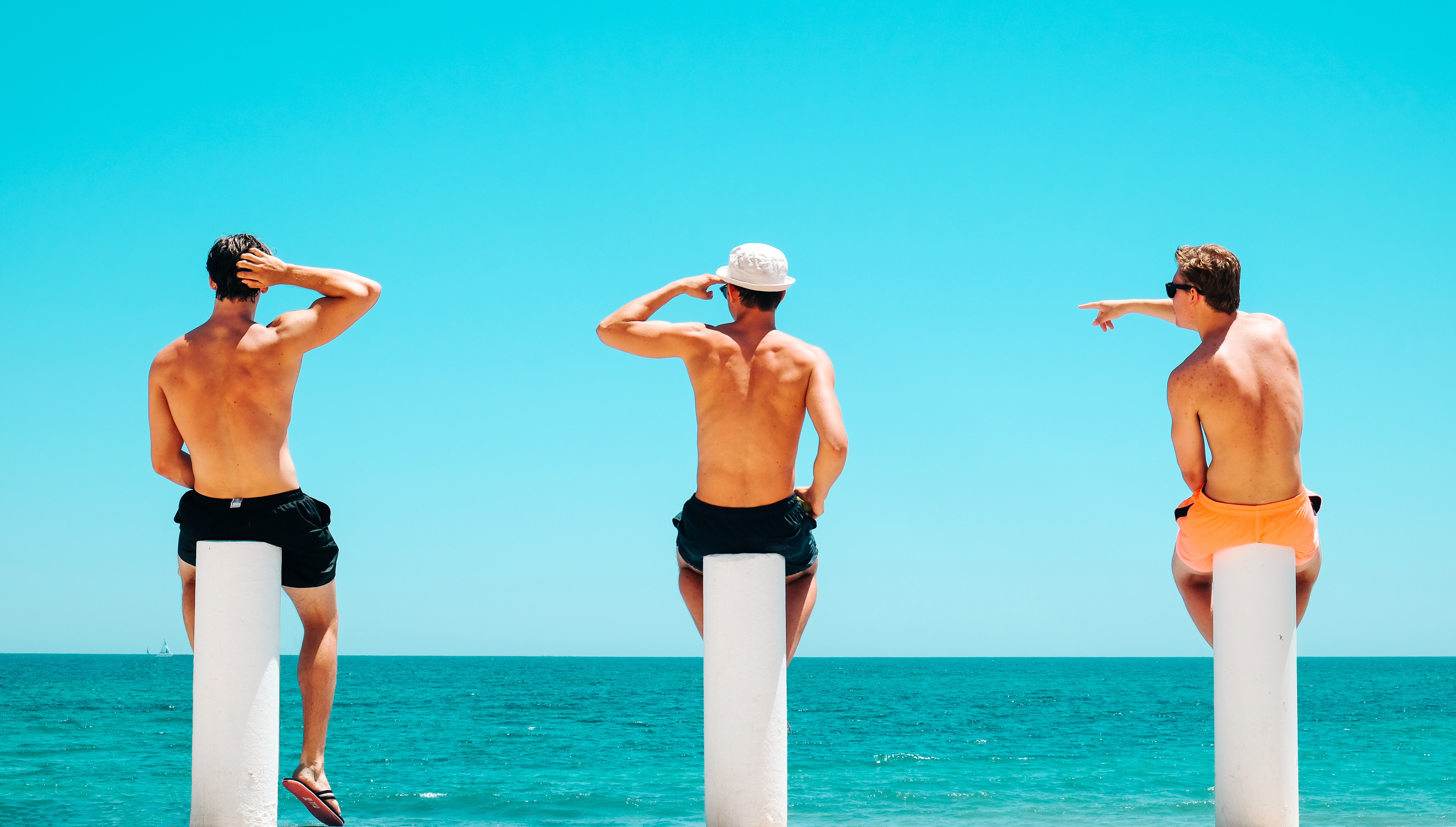 Three men sitting on poles by the Mediterranean Sea HD Wallpaper