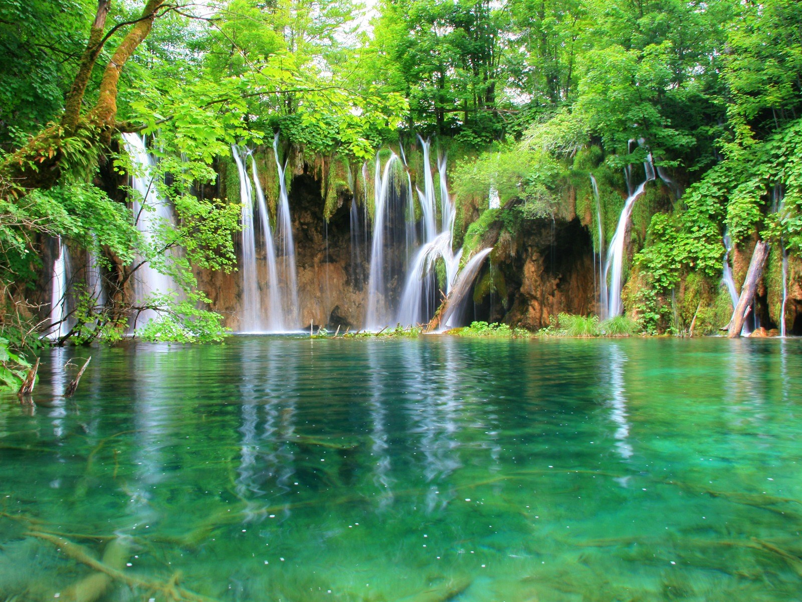 Waterfalls cascading into a clear green lake HD Wallpaper