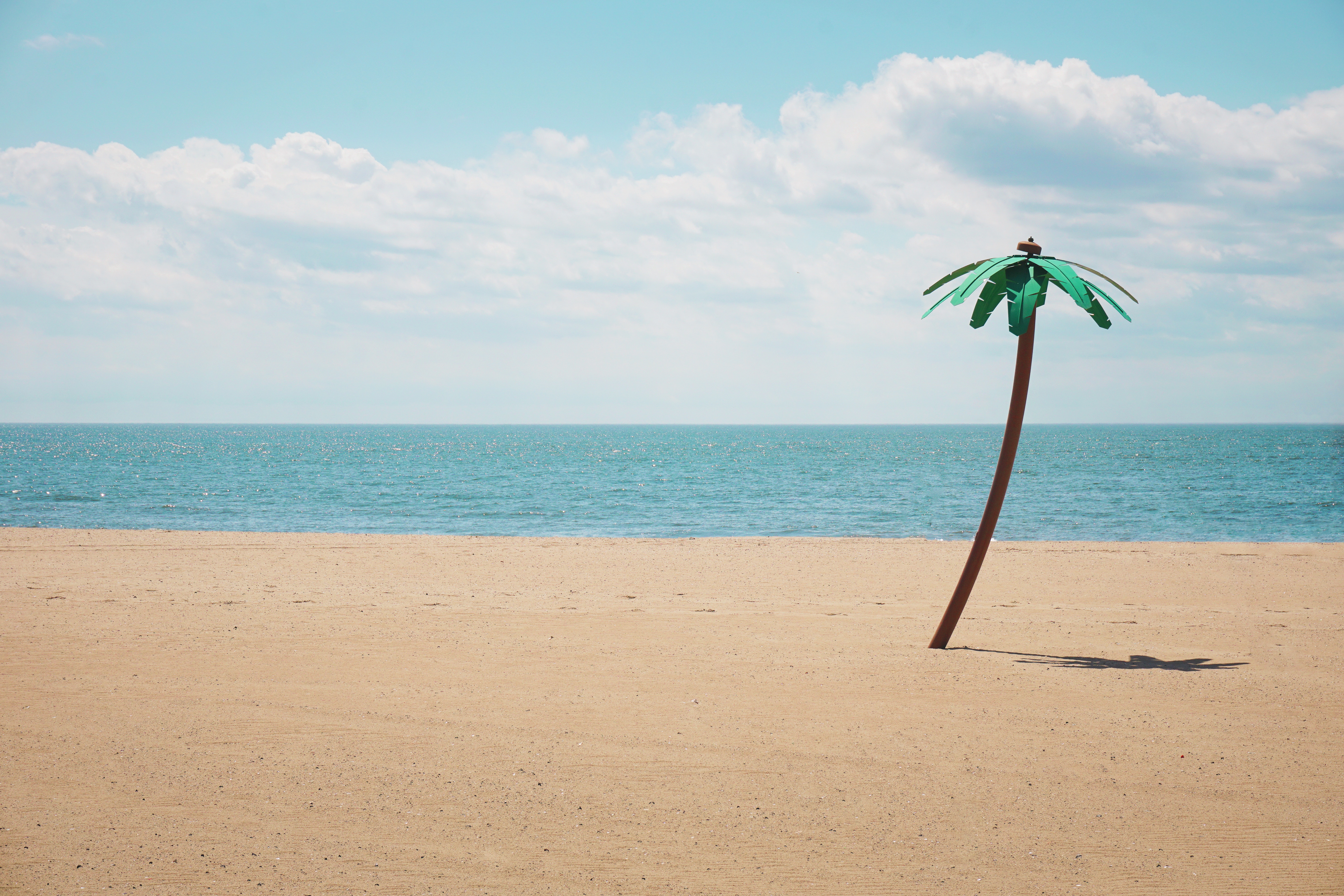 Fake palm tree on a sandy beach with ocean and clouds HD Wallpaper