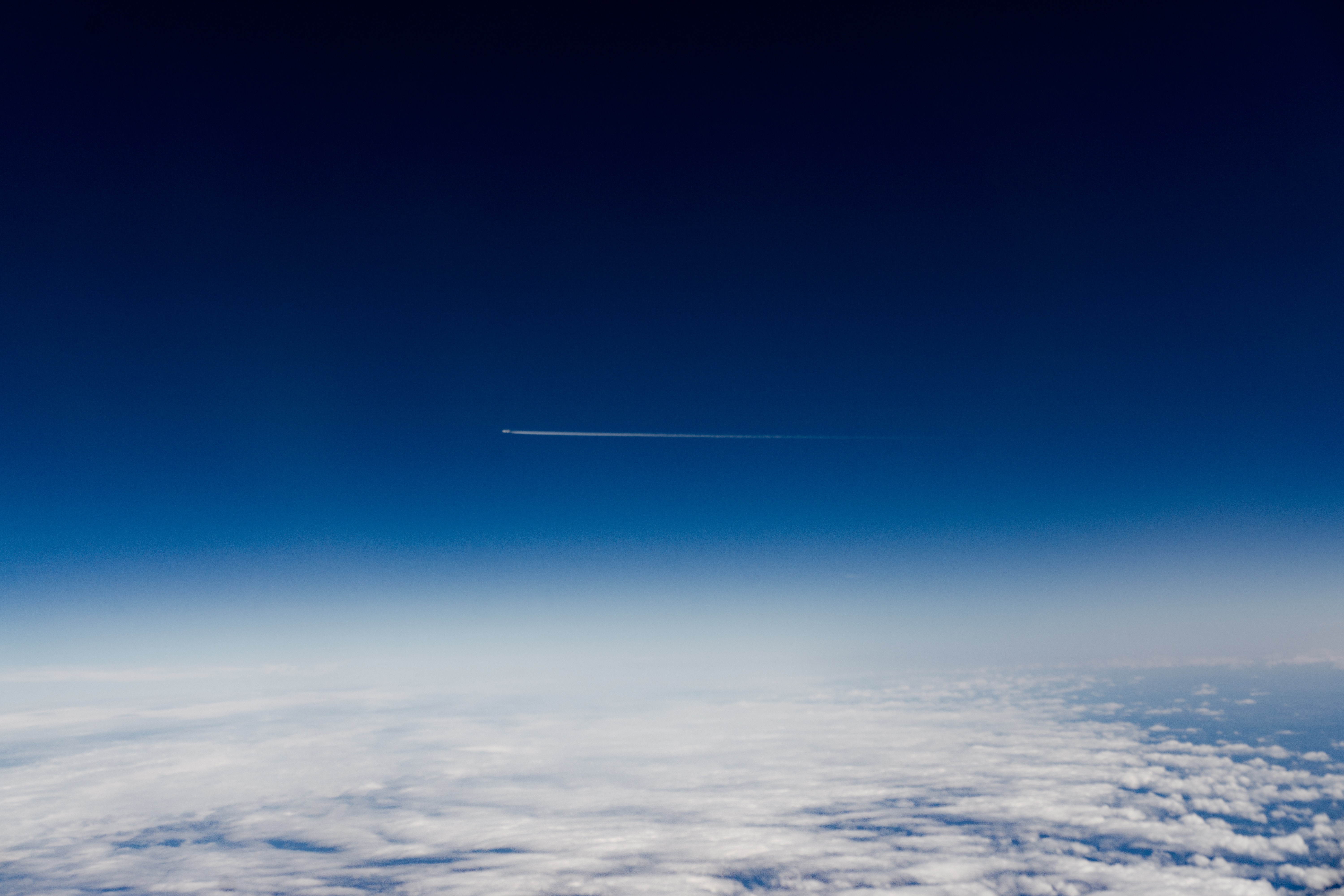 Airplane contrail in a clear blue sky above clouds HD Wallpaper