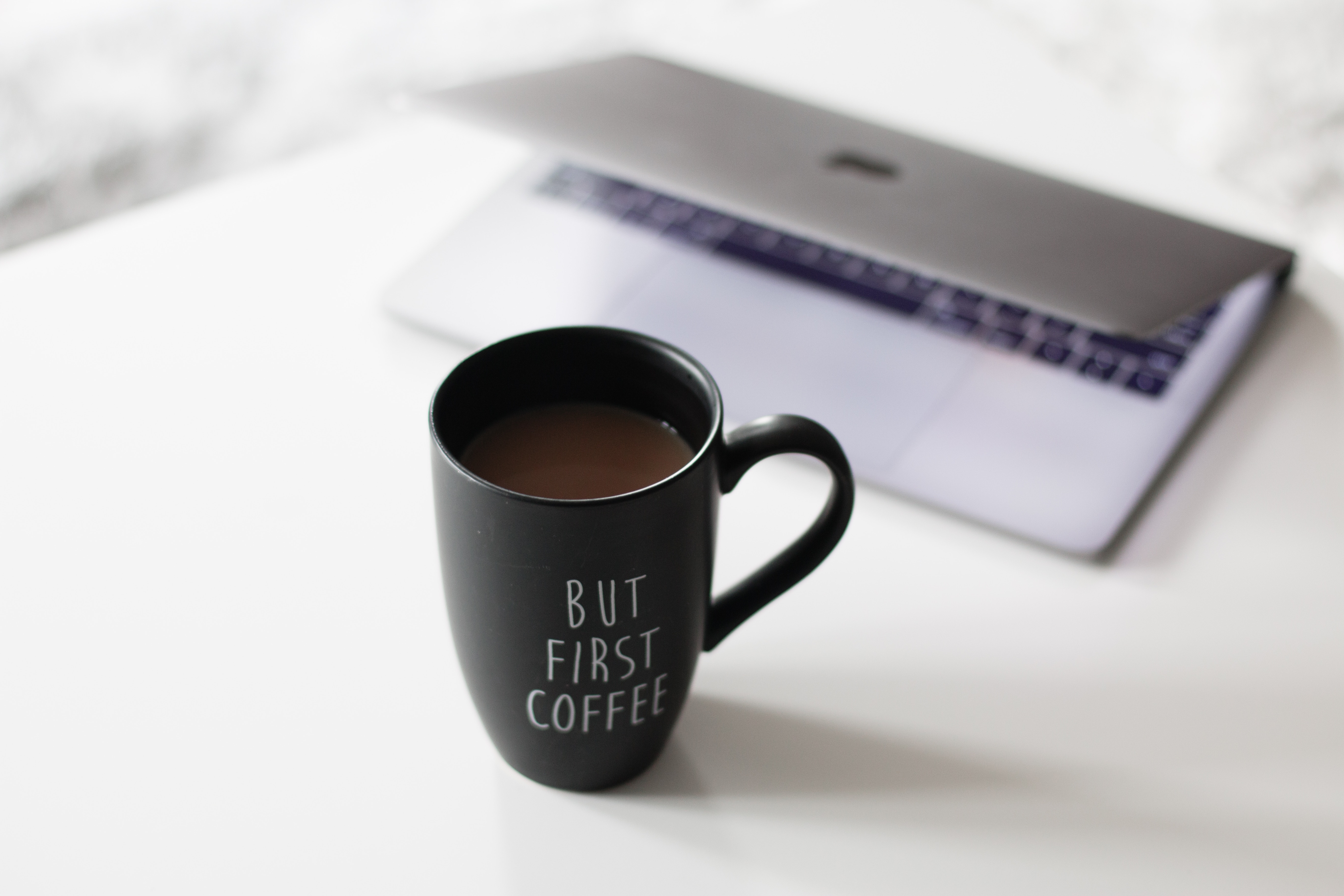 Black coffee mug with text and MacBook on a white table HD Wallpaper