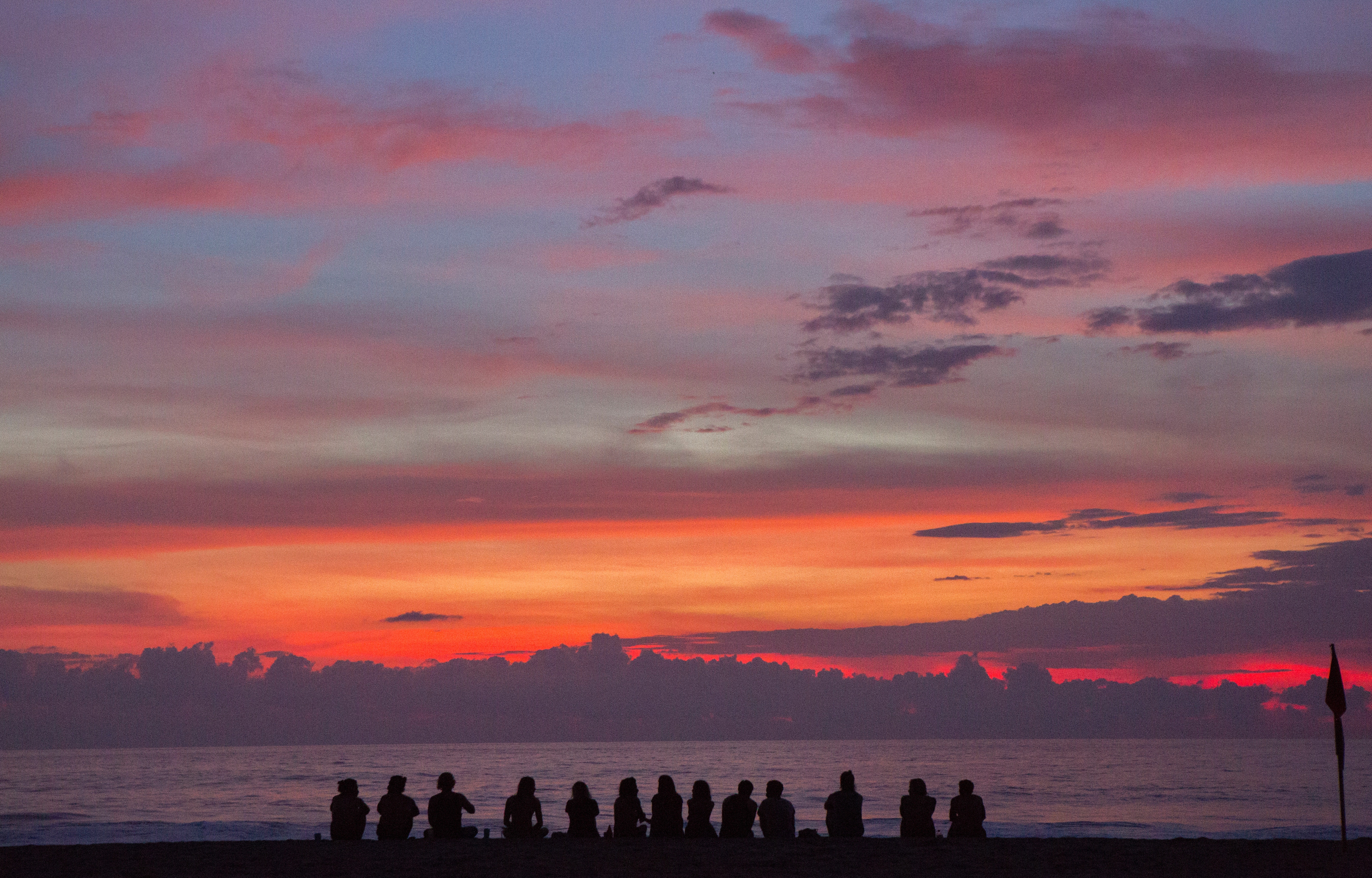 Silhouetted group watching vibrant beach sunset HD Wallpaper
