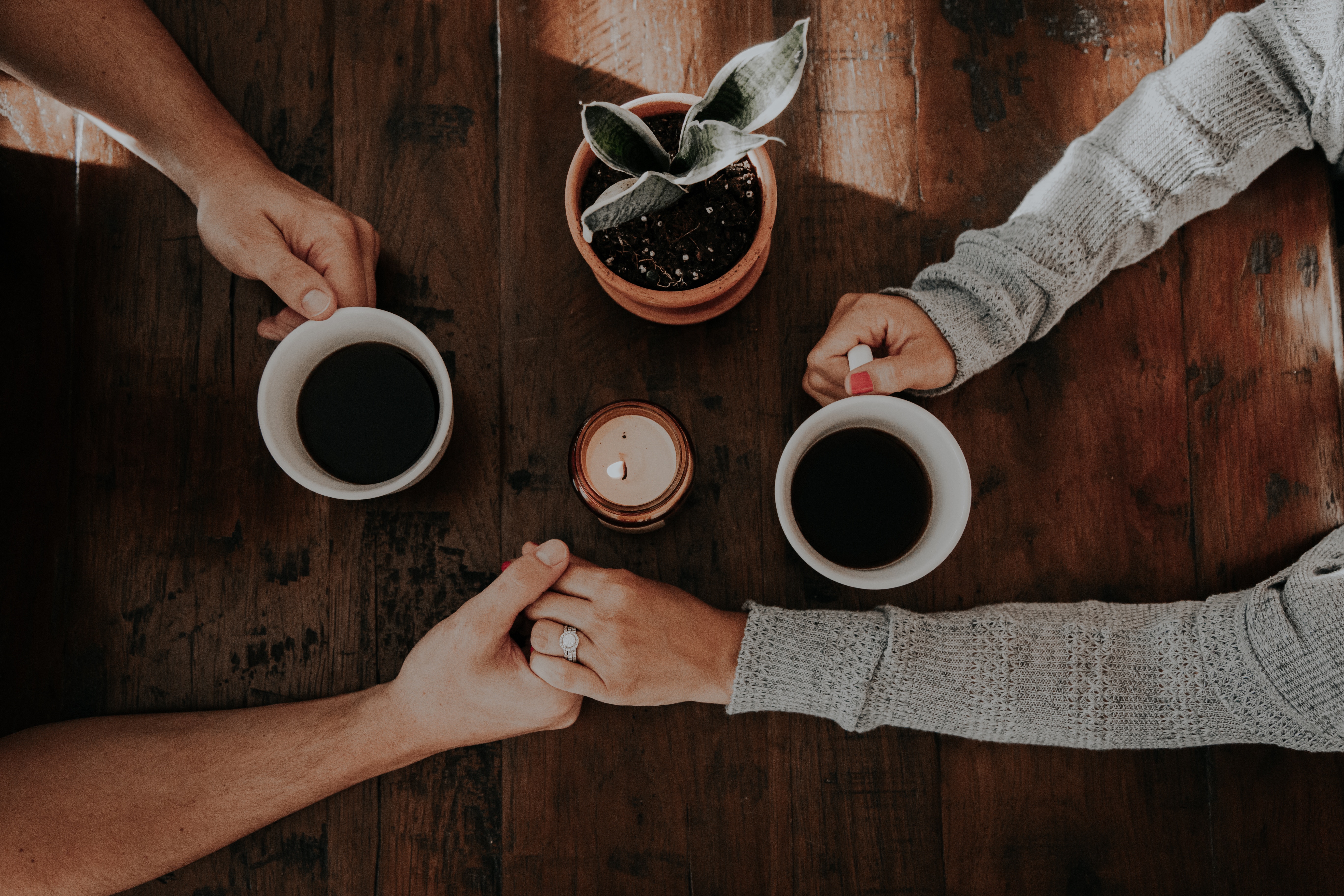 Couple holding hands and drinking coffee on a wooden table HD Wallpaper