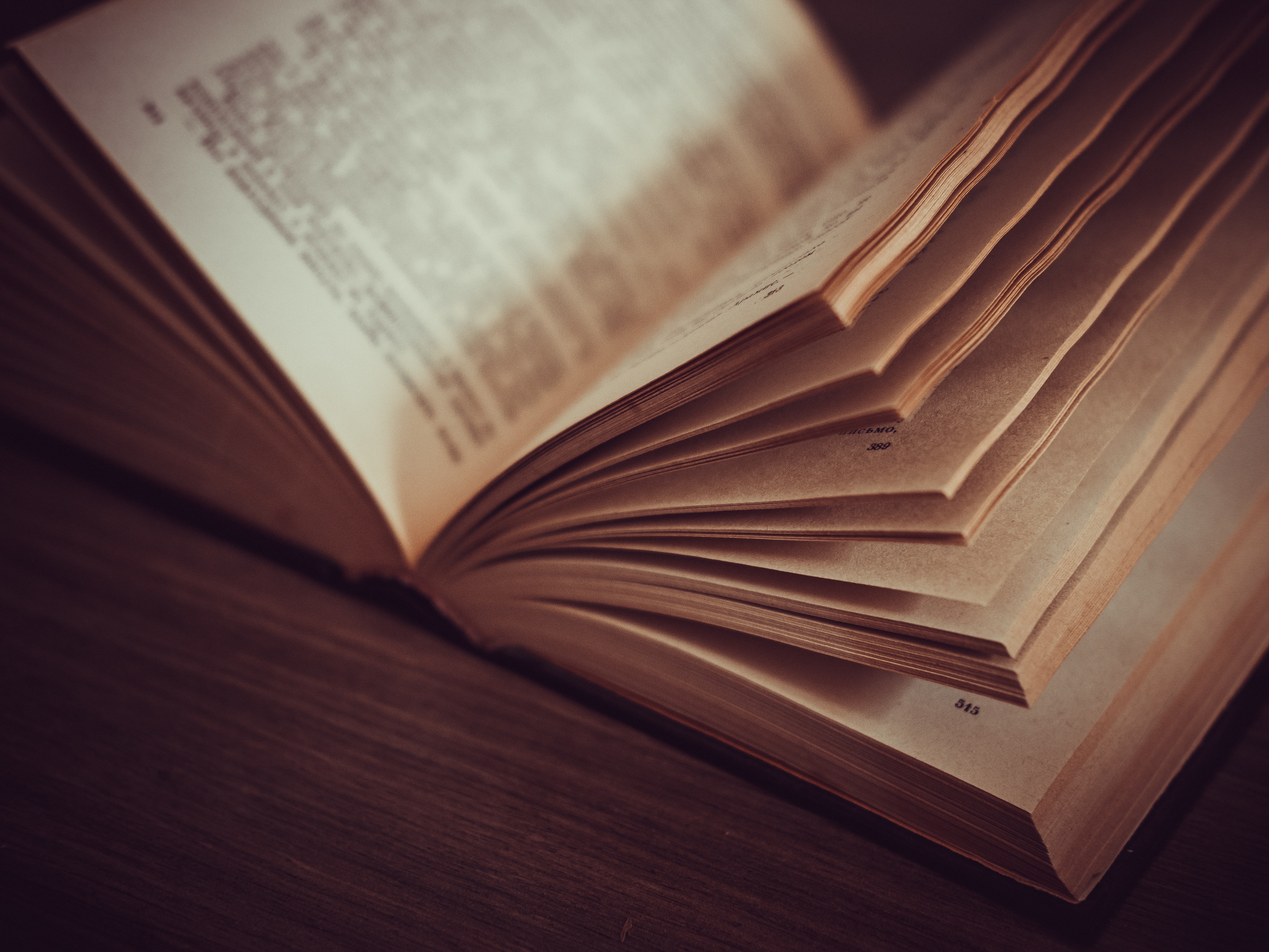 Open book with pages fanned out on a wooden table HD Wallpaper