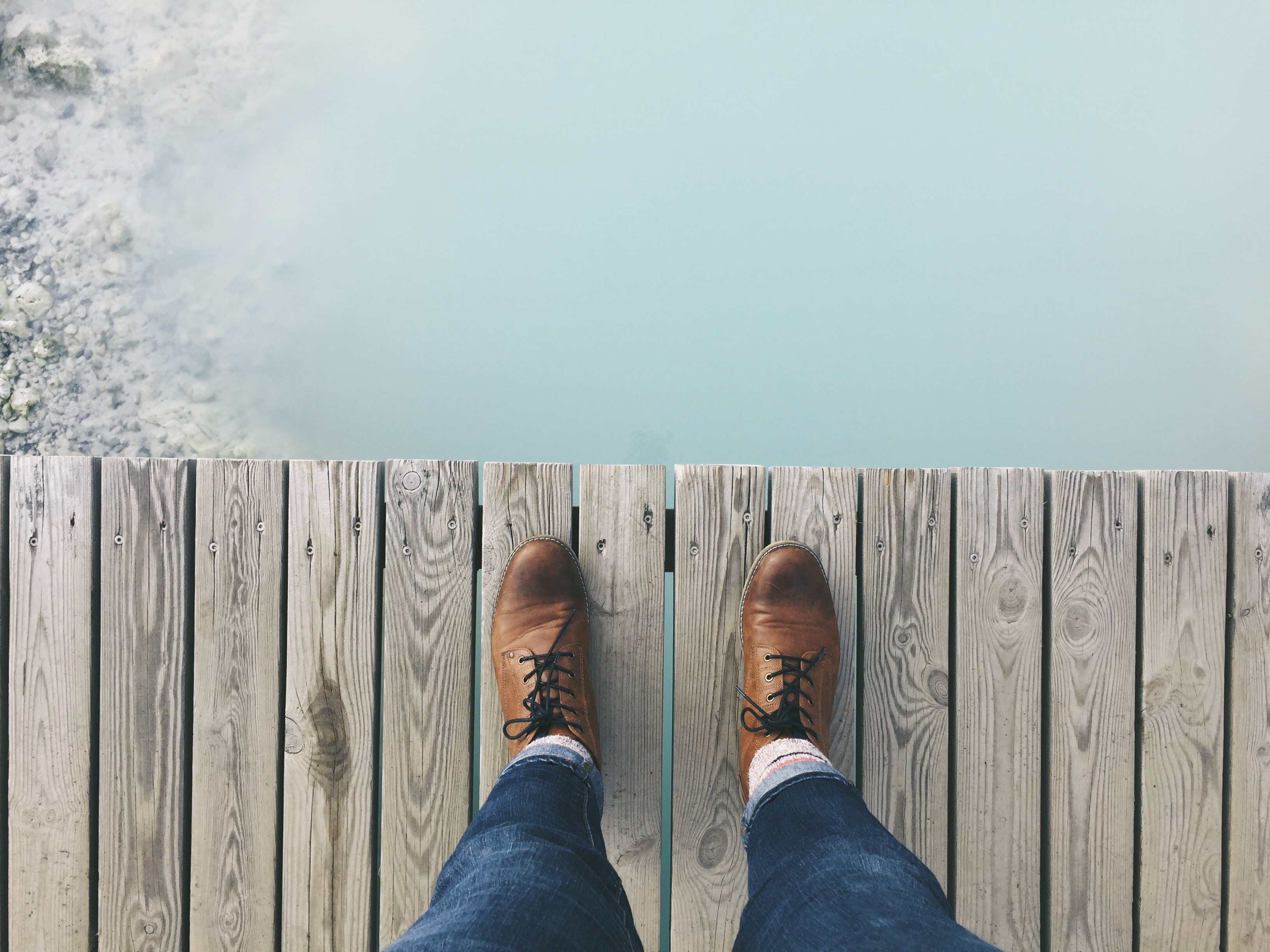 Feet on a wooden boardwalk overlooking a blue lagoon HD Wallpaper