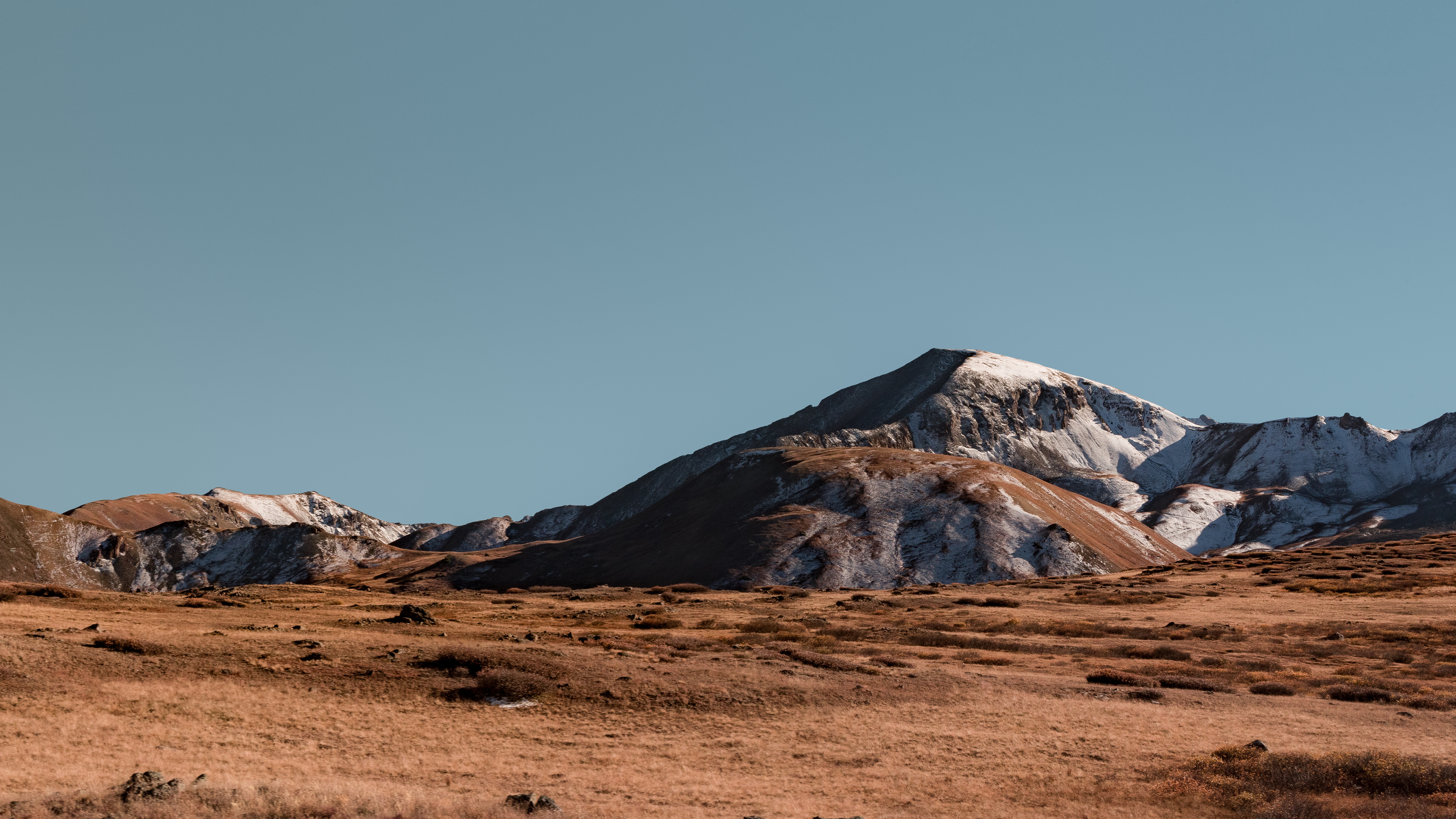 Mountain range with snow and dry grass under blue sky HD Wallpaper