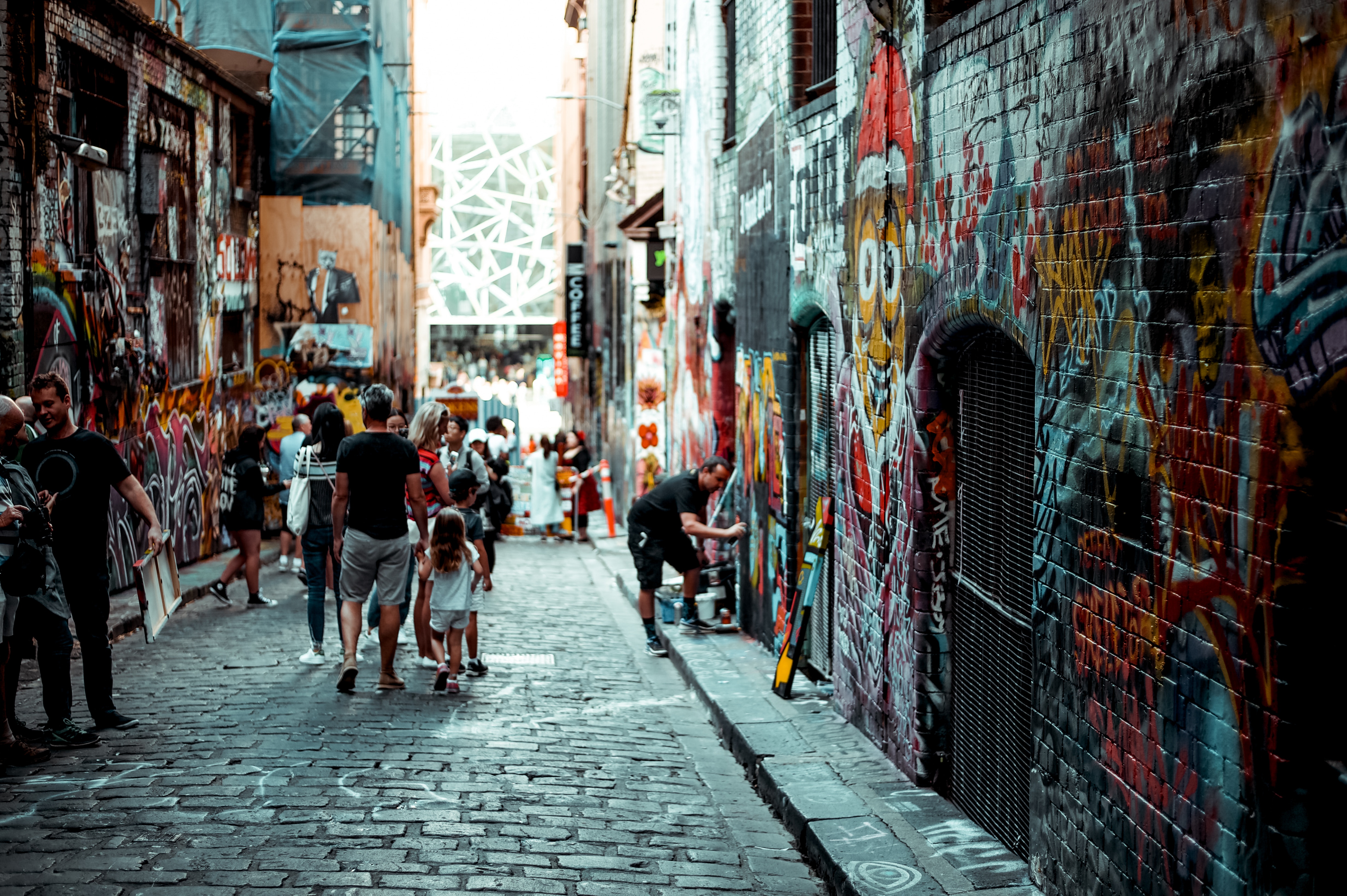 People walk down a graffiti-covered alleyway HD Wallpaper