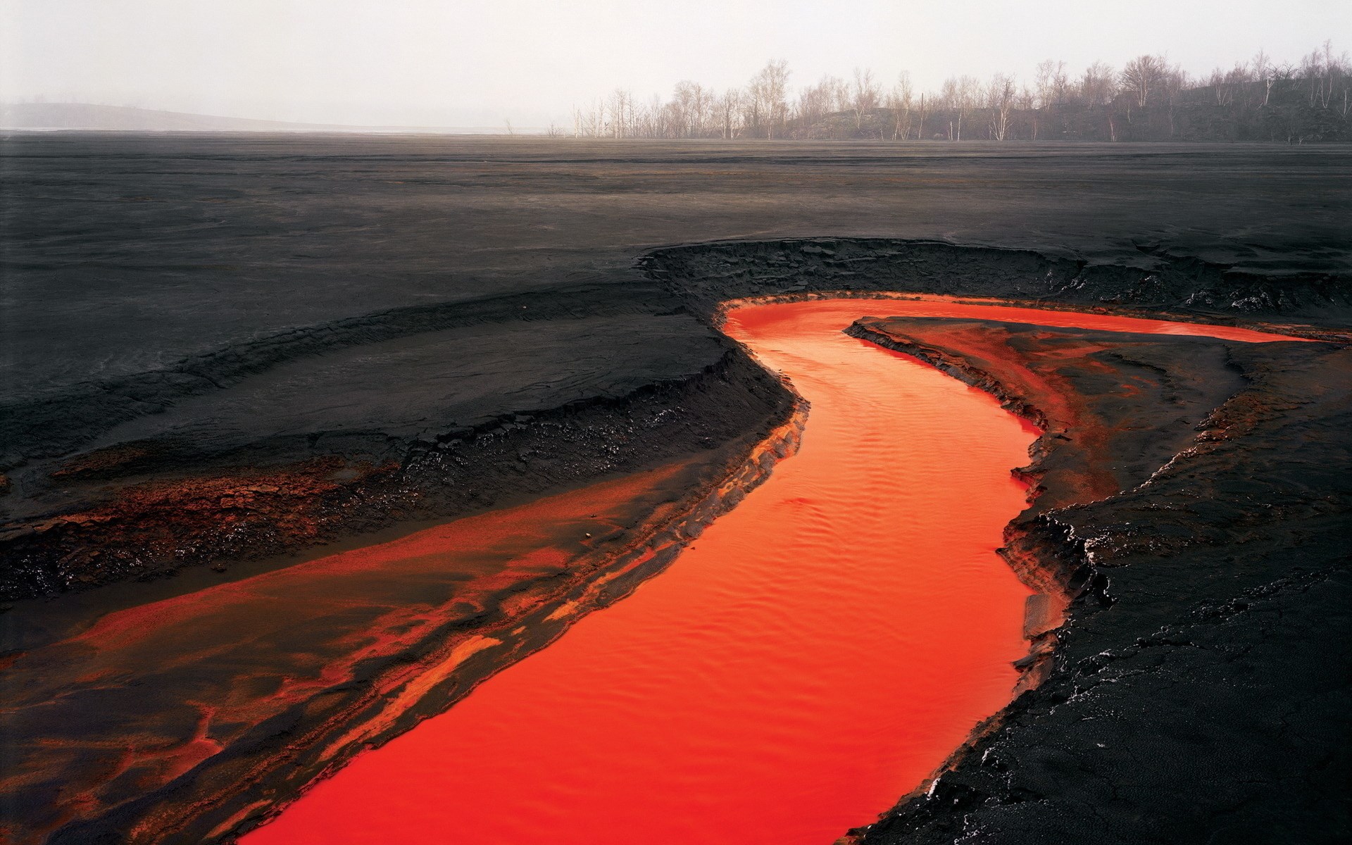 Red river flowing through black industrial landscape HD Wallpaper