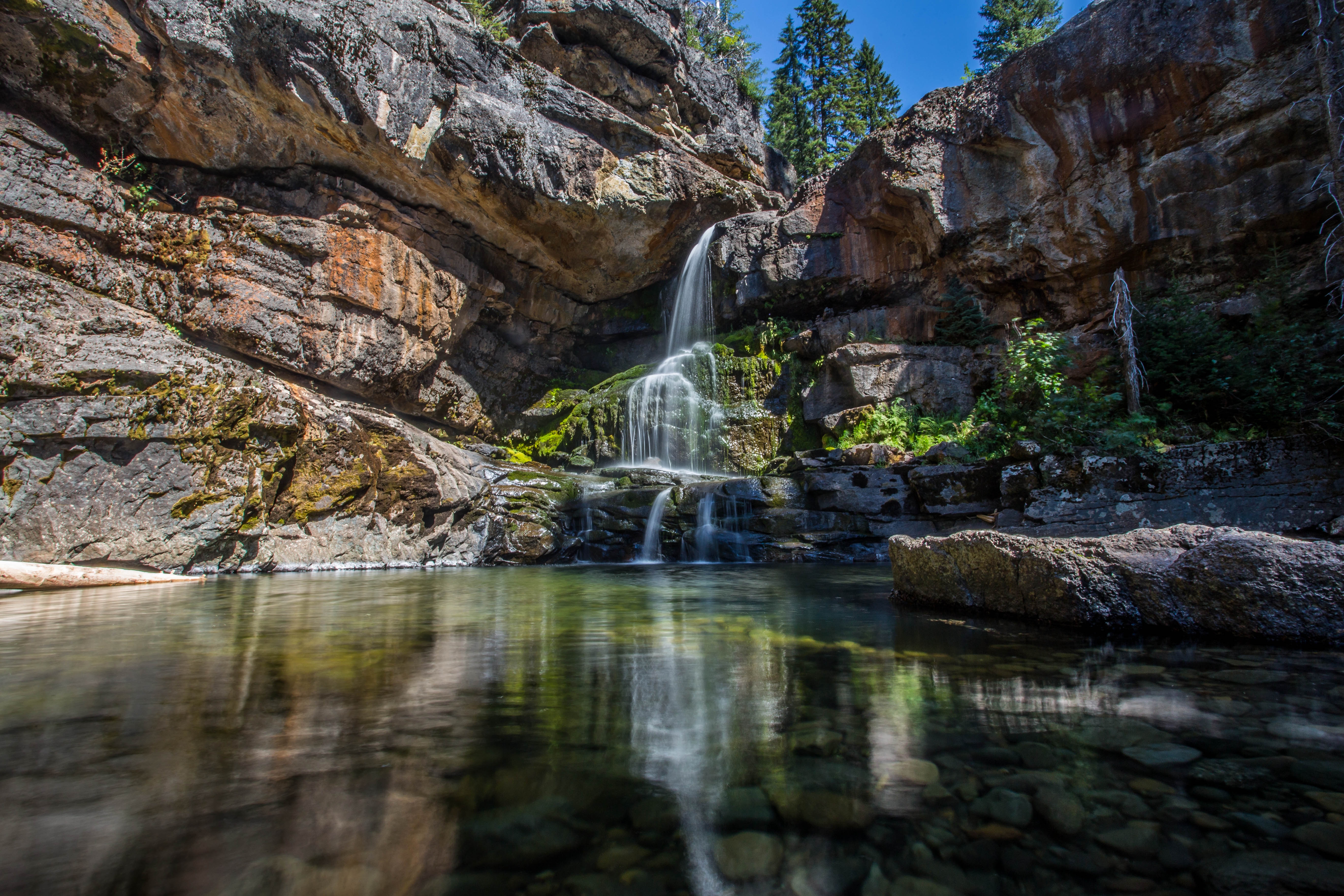 Waterfall cascading into a clear pool surrounded by rocky cliffs HD Wallpaper