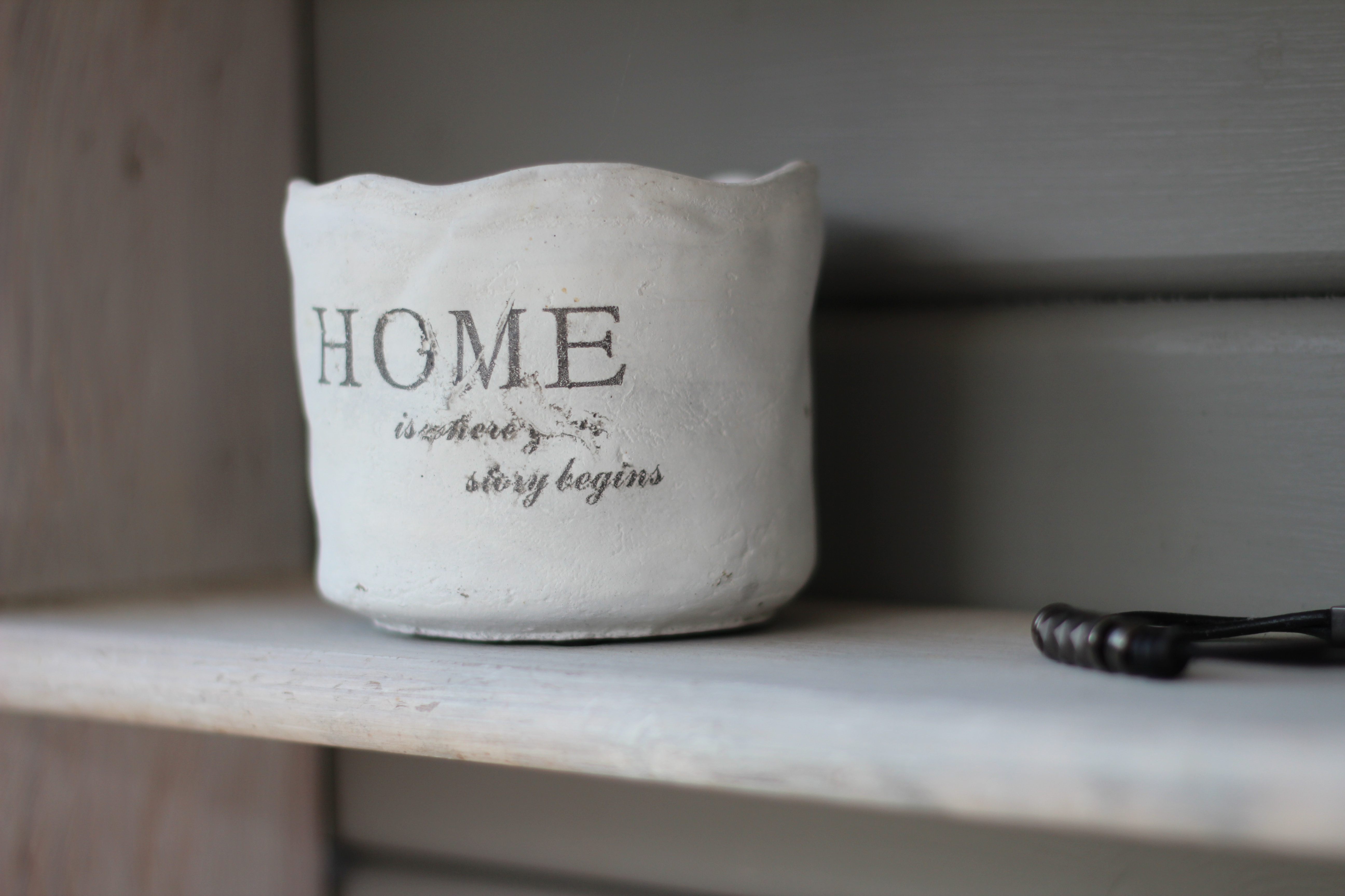 White pot with "HOME is where the story begins" text on a shelf HD Wallpaper