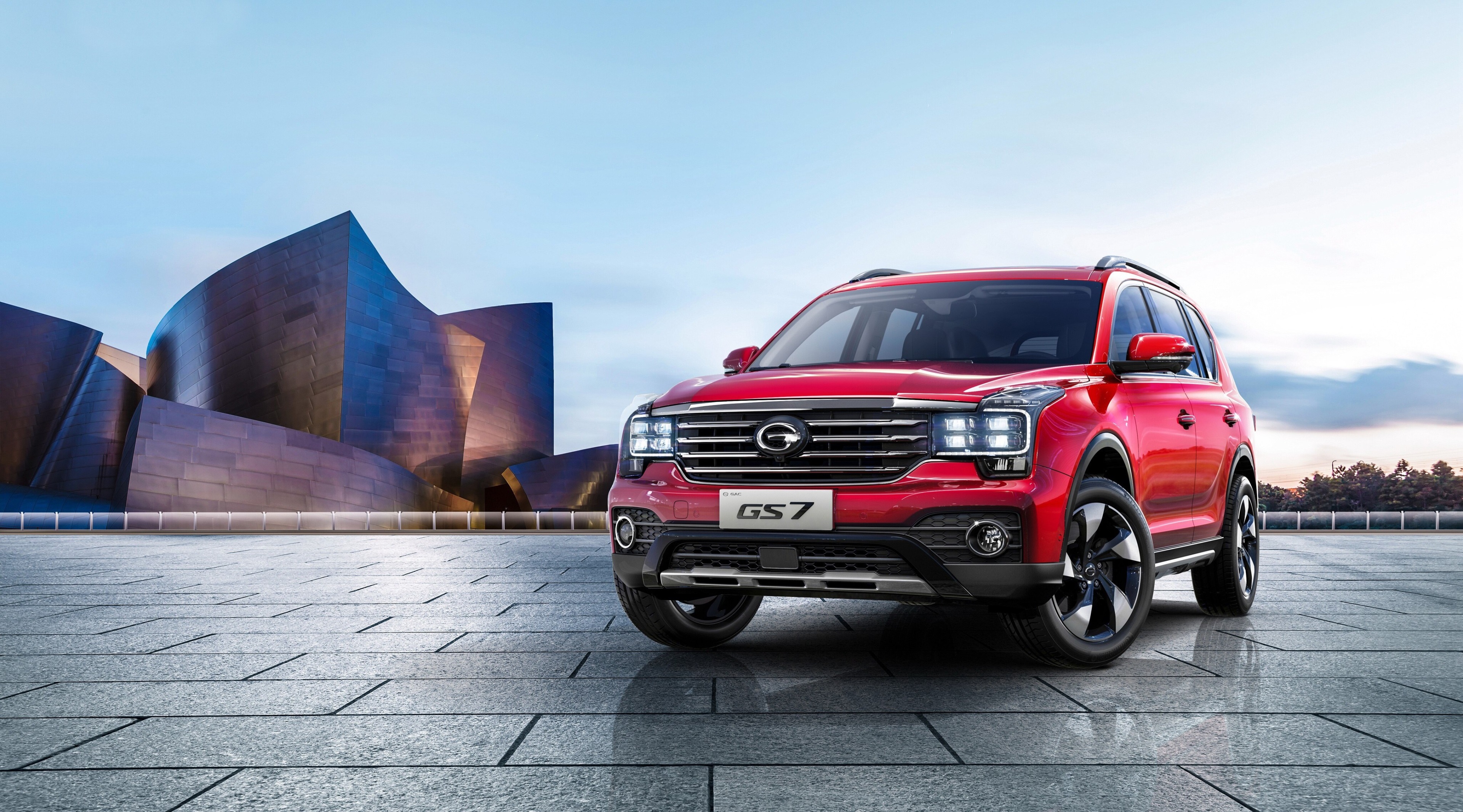 Red GAC Trumpchi GS7 SUV in front of modern architecture HD Wallpaper