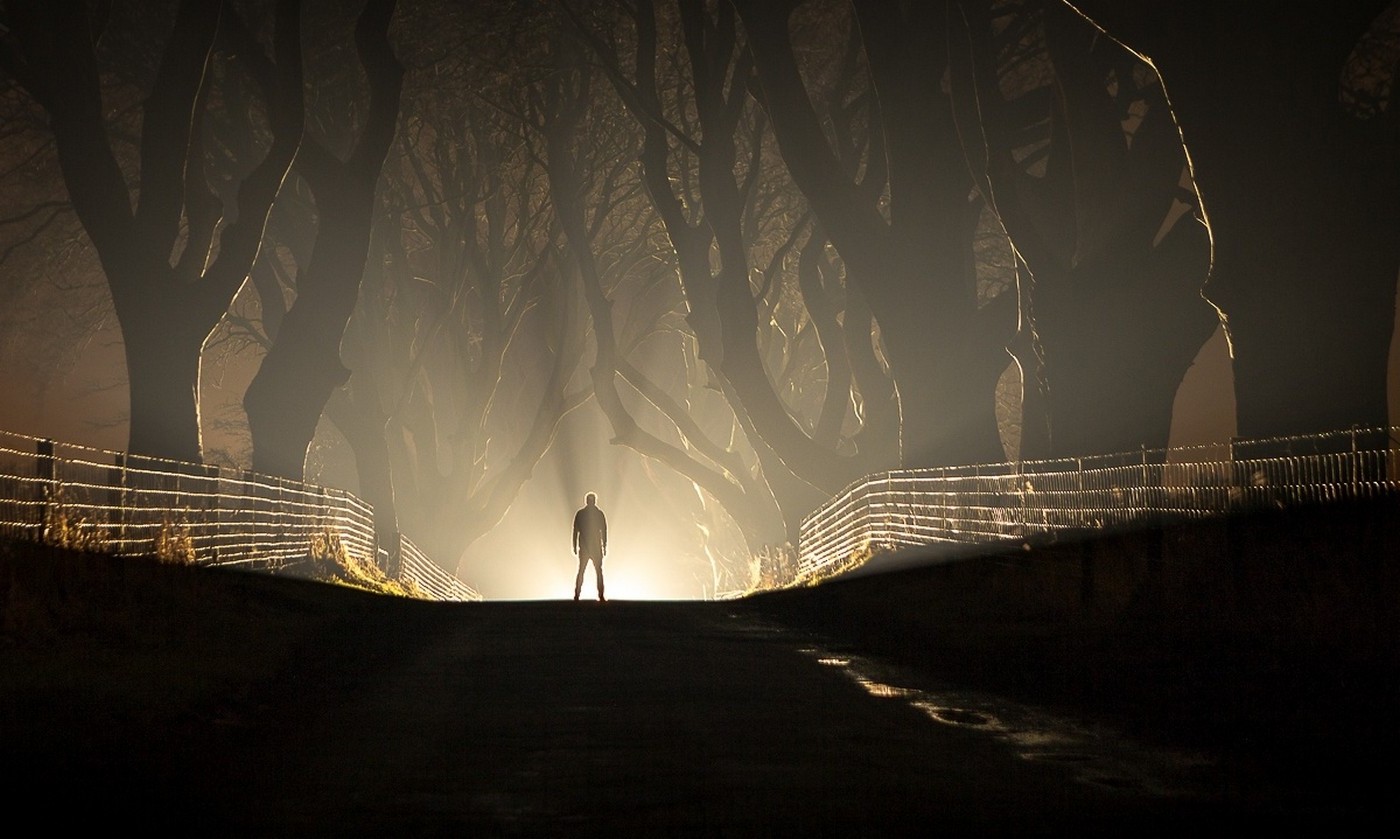 Man standing on a road at night with trees and mist HD Wallpaper