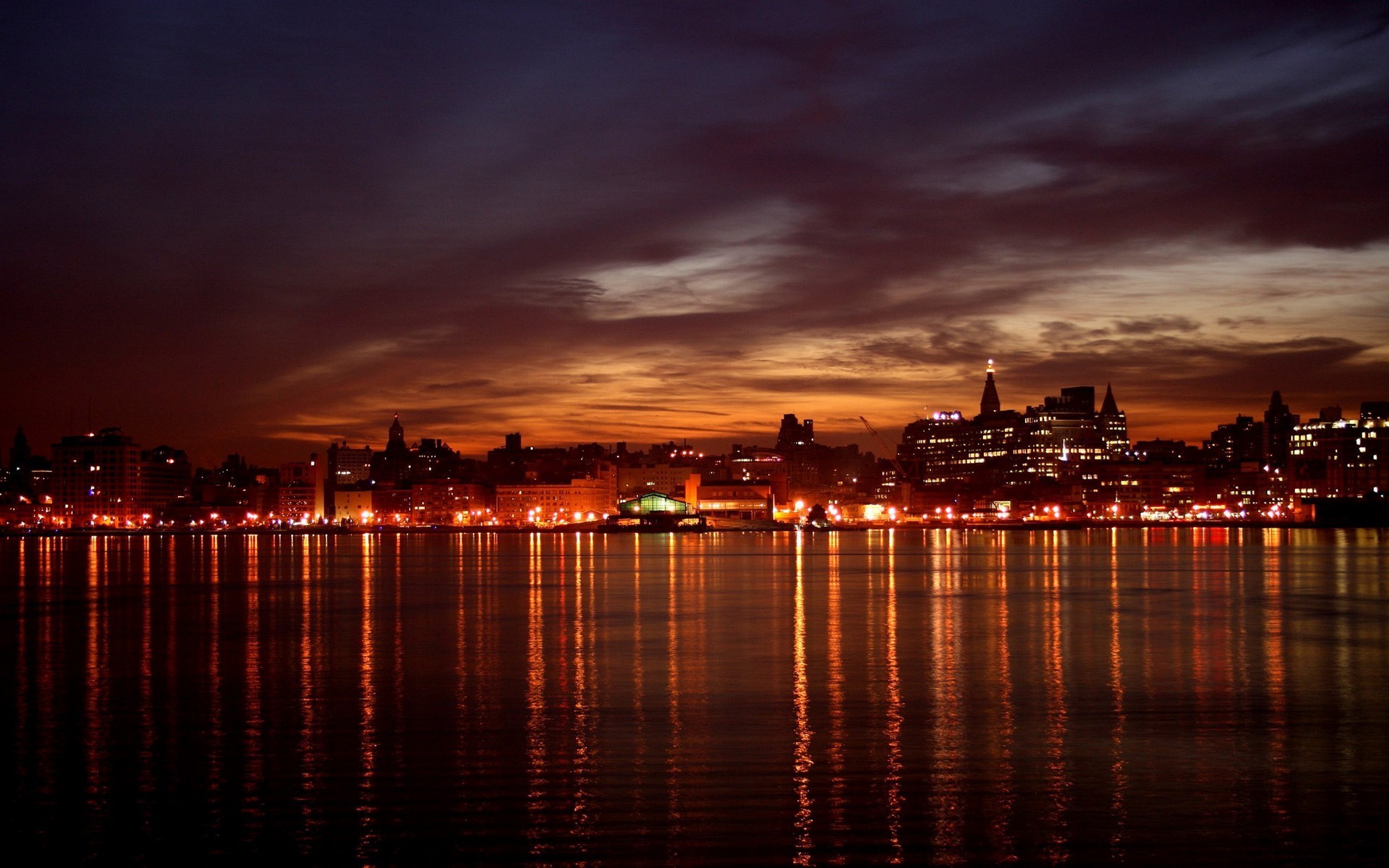 City skyline at night with water reflections HD Wallpaper
